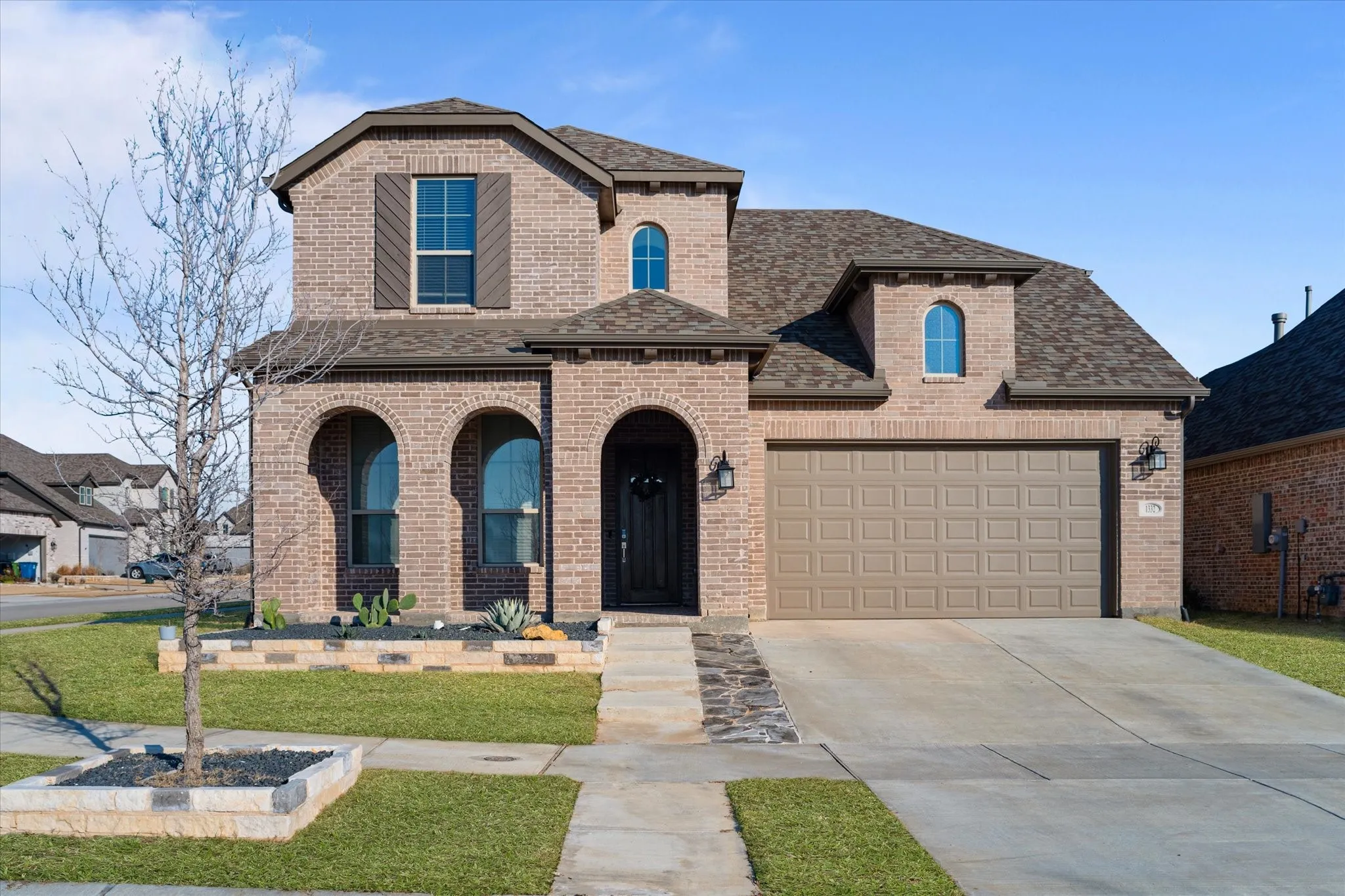 Brick facade with arched entryways, attached two-car garage, and a gabled roofline
