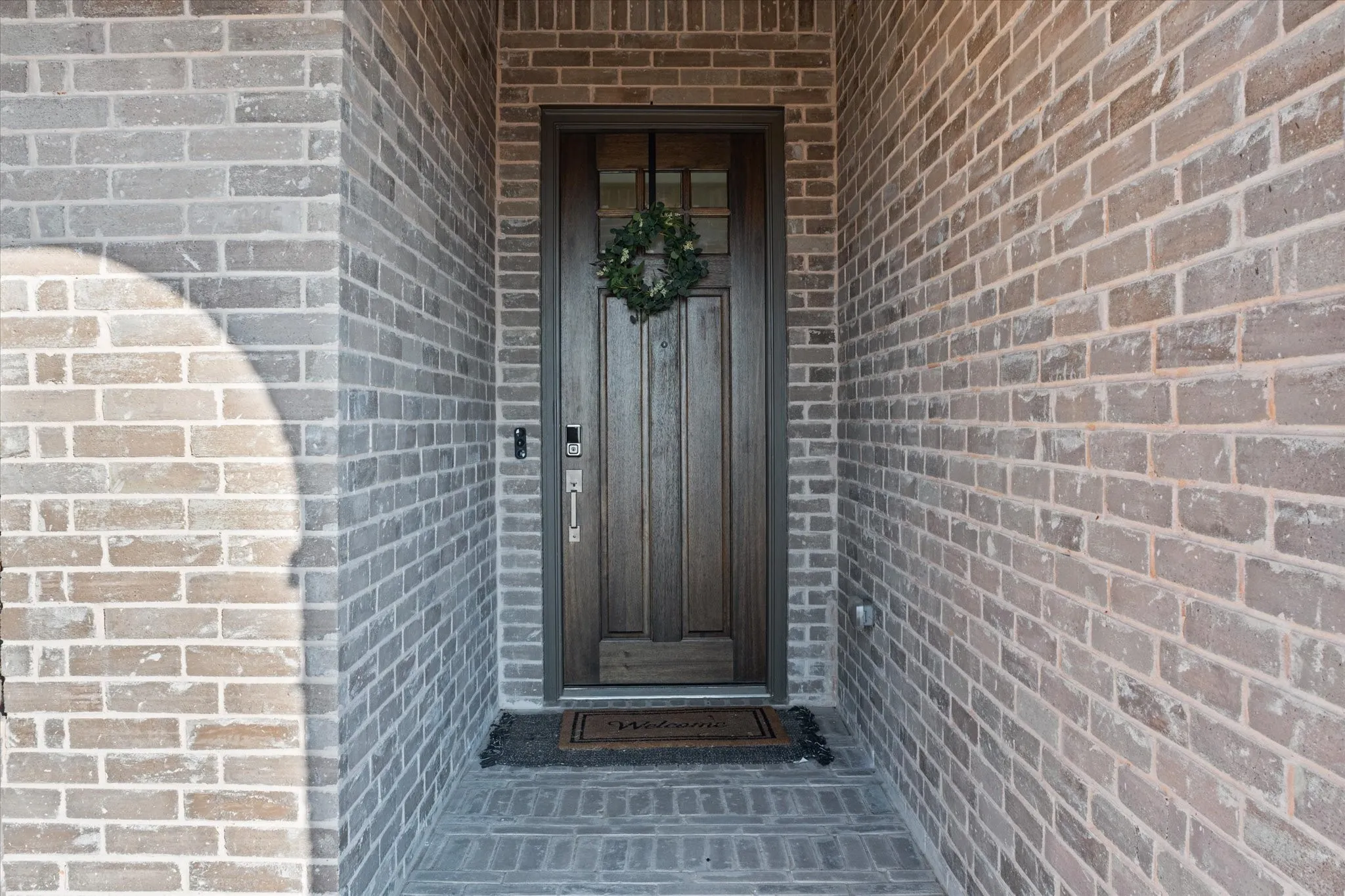Brick facade with a solid wood entry door, integrated transom window, and brick-laid entryway