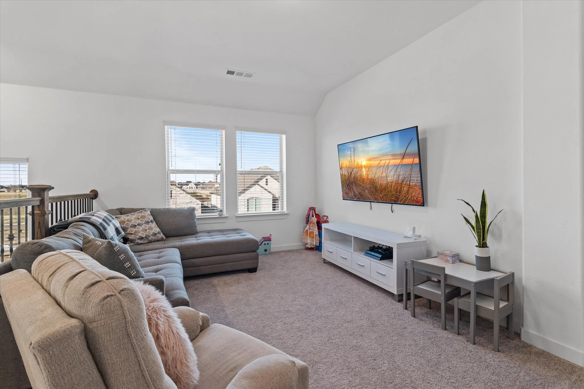Carpeted room with white walls, multiple windows, and a wood and metal railing