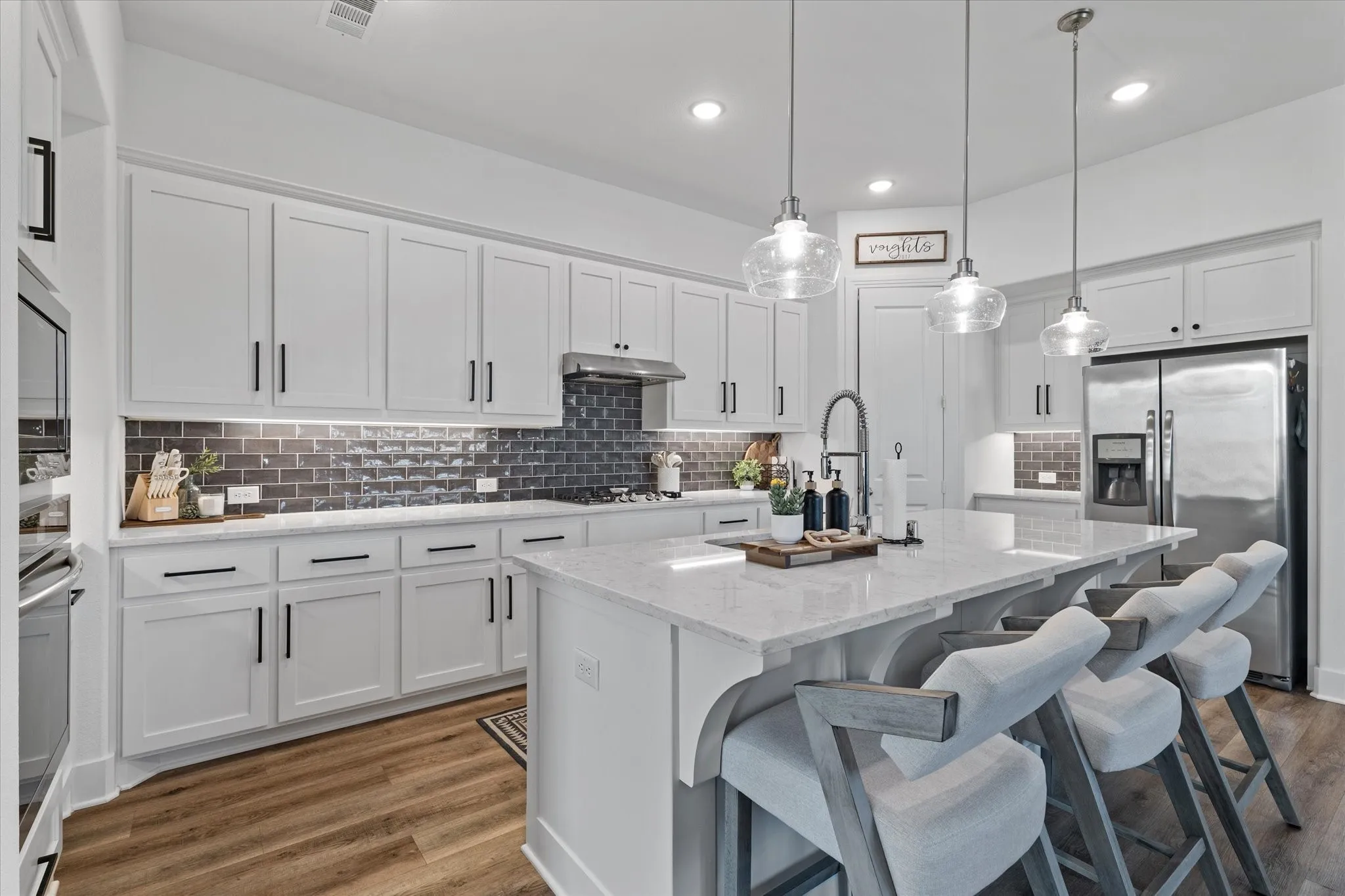 White cabinetry with black hardware, stainless steel appliances, marble-finish countertops, subway tile backsplash, and wood-finish flooring