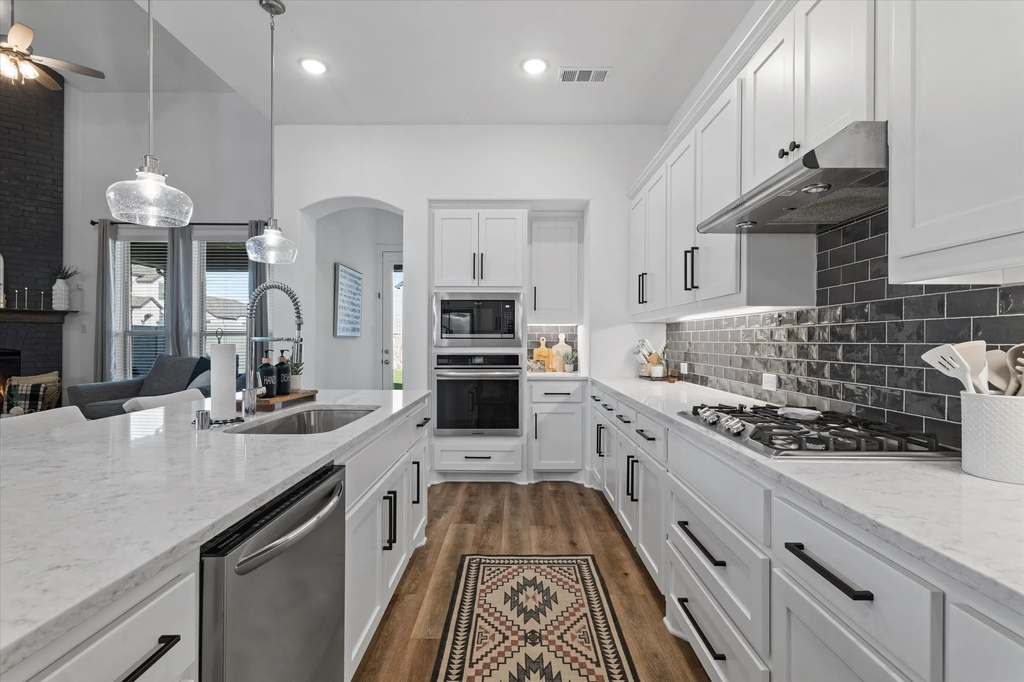 Kitchen featuring white cabinetry, light-toned countertops, stainless steel appliances, a dark subway tile backsplash, and wood-finish flooring