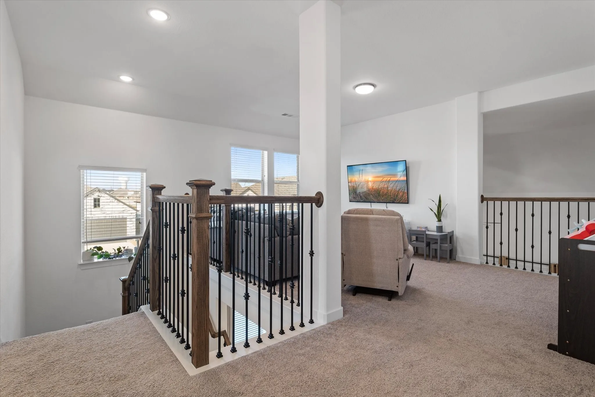 Carpeted loft area with recessed lighting, multiple windows, and dark wood newel posts with black iron balusters