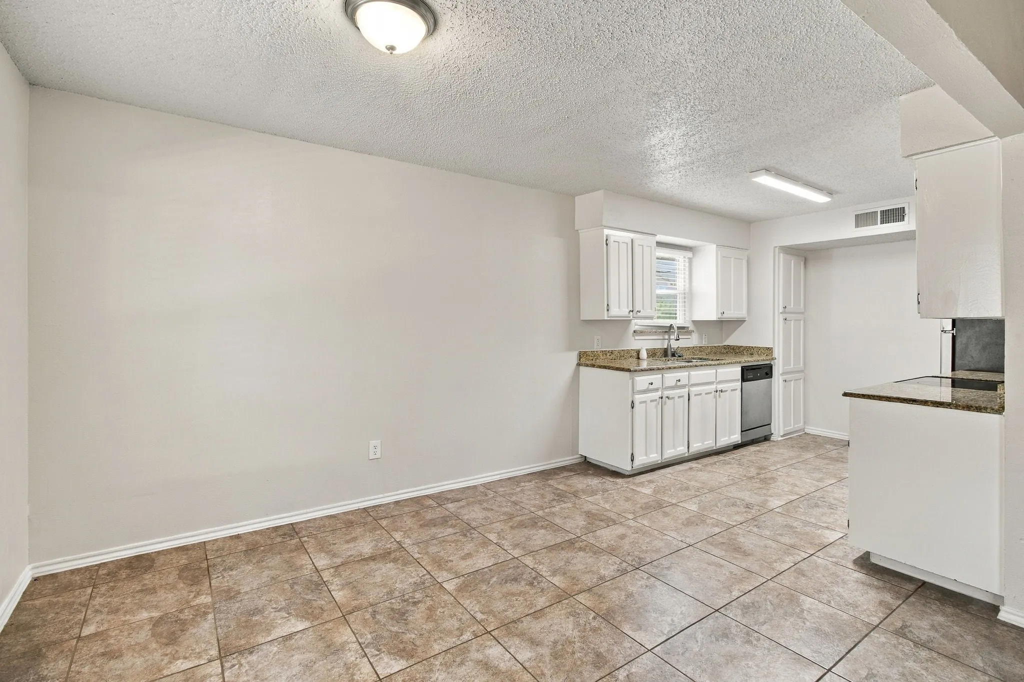 Tile flooring, white cabinetry, integrated dishwasher, and stone-finish countertops