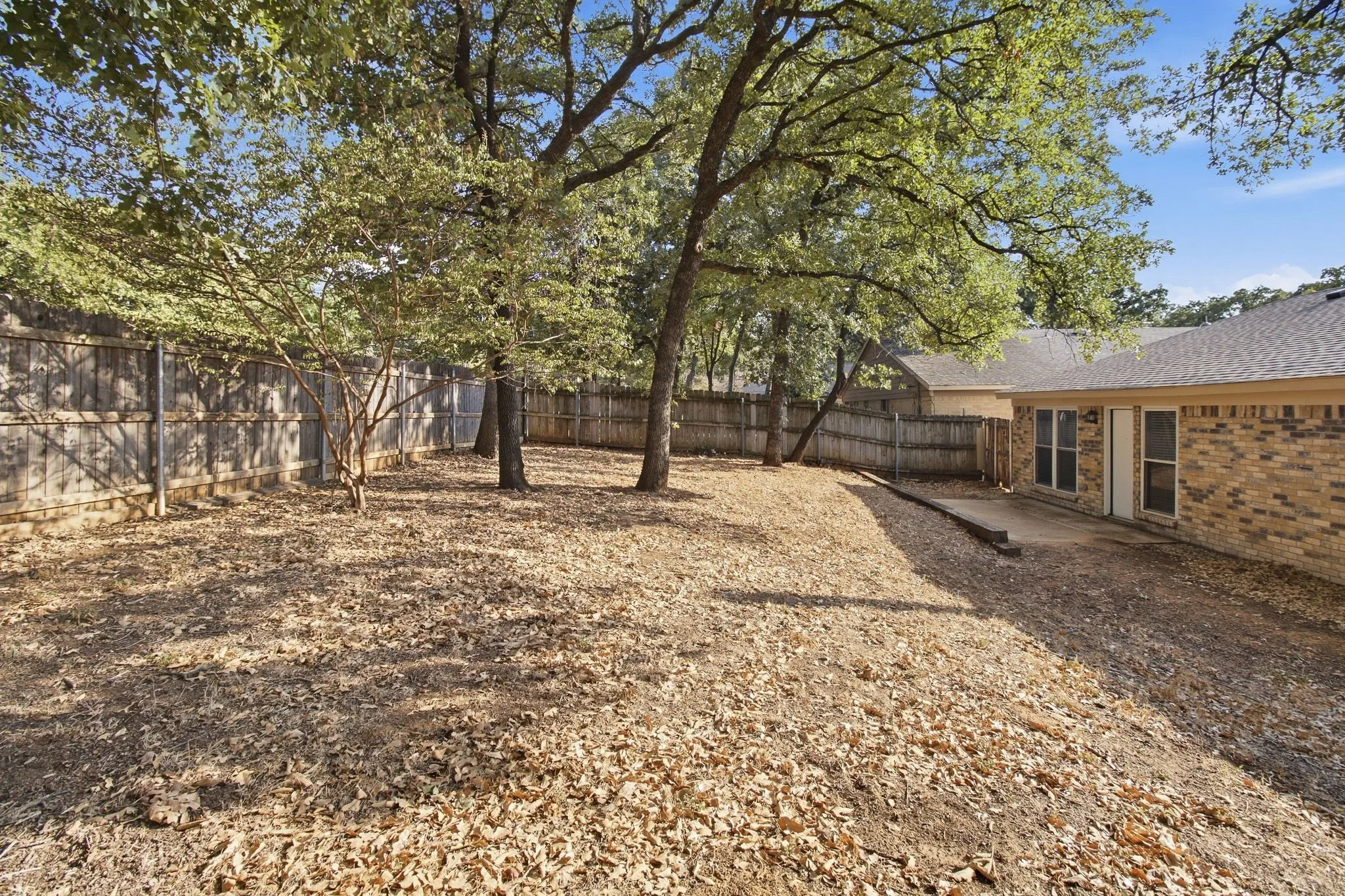 Expansive backyard featuring mature trees, a wood privacy fence, and a concrete patio