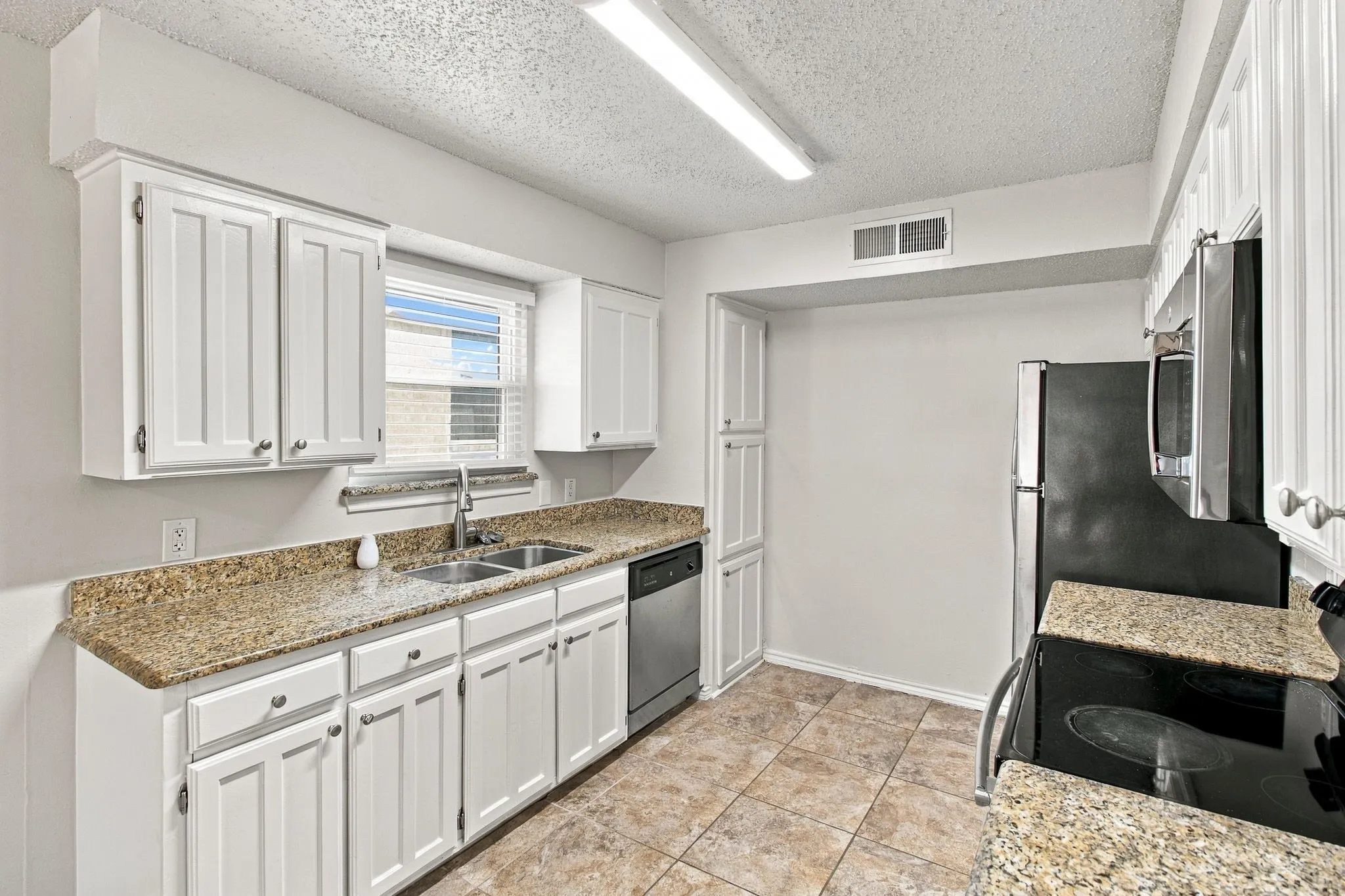 Kitchen featuring white cabinetry, granite countertops, tile flooring, a double basin sink, and stainless steel appliances