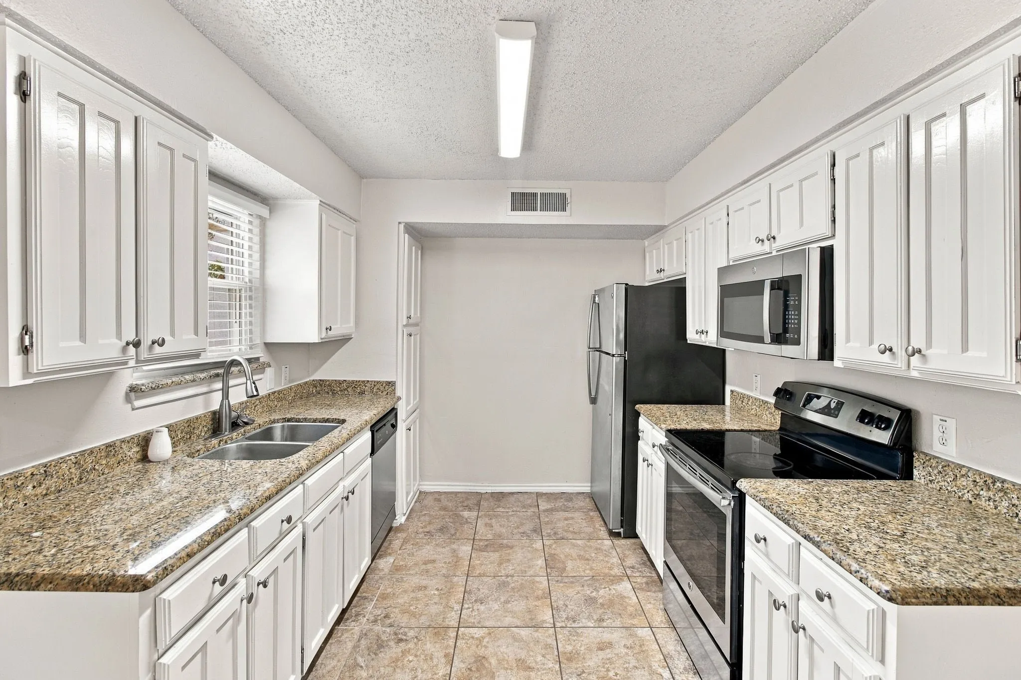 White cabinetry, dual basin stainless steel sink, tile flooring, granite-style countertops, and a built-in microwave