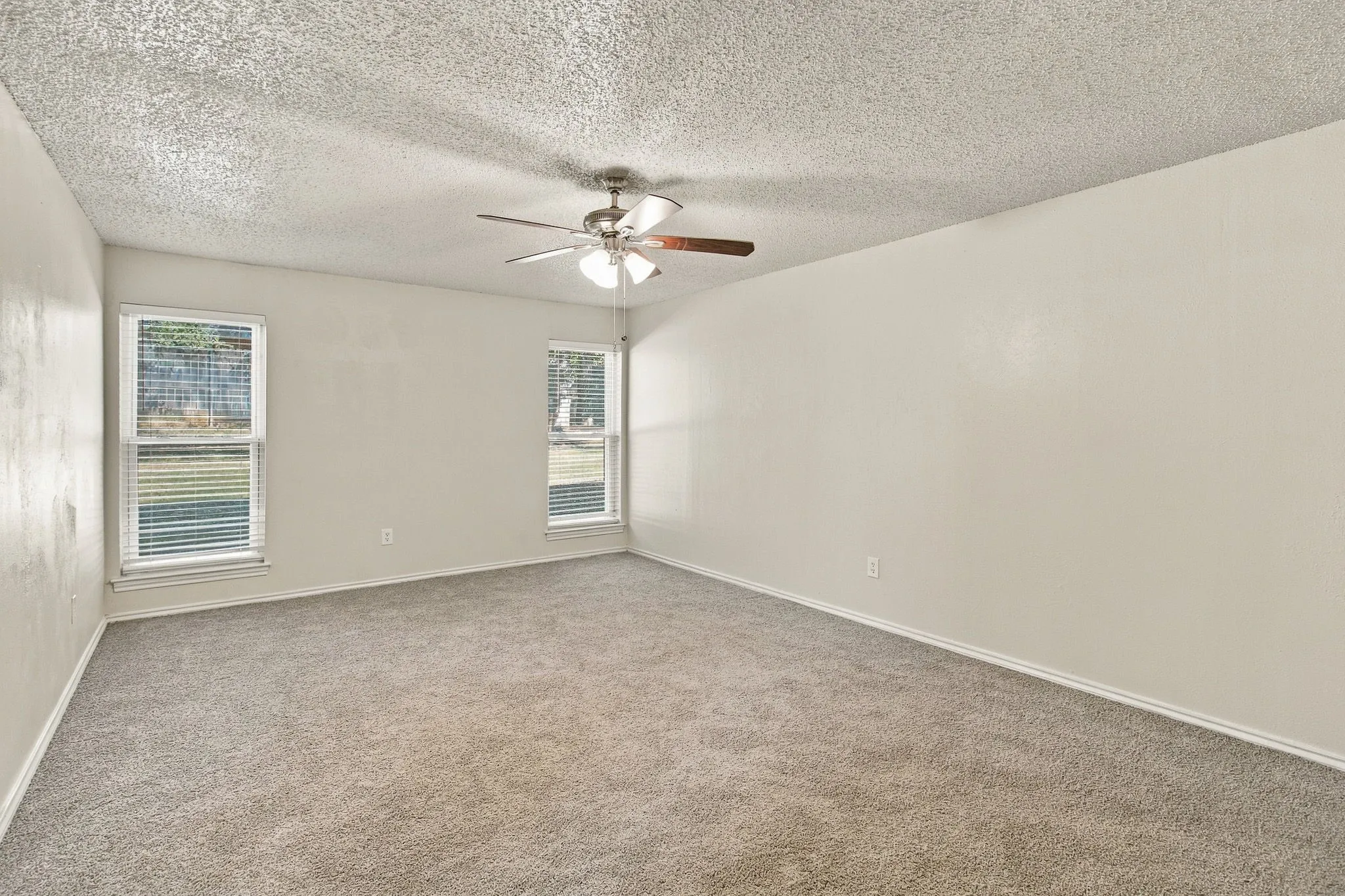 Spacious room featuring neutral paint, textured ceiling, two windows with blinds, and a ceiling fan
