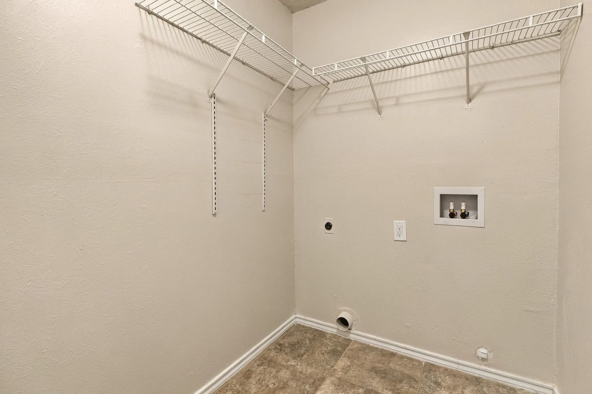 Utility area featuring durable tile flooring, white wire shelving, and appliance hookups