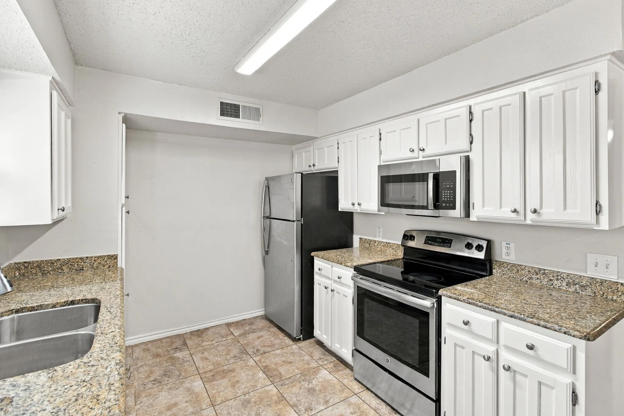White cabinetry, stainless steel appliances, stone-finish countertops, tile flooring, and a double basin sink