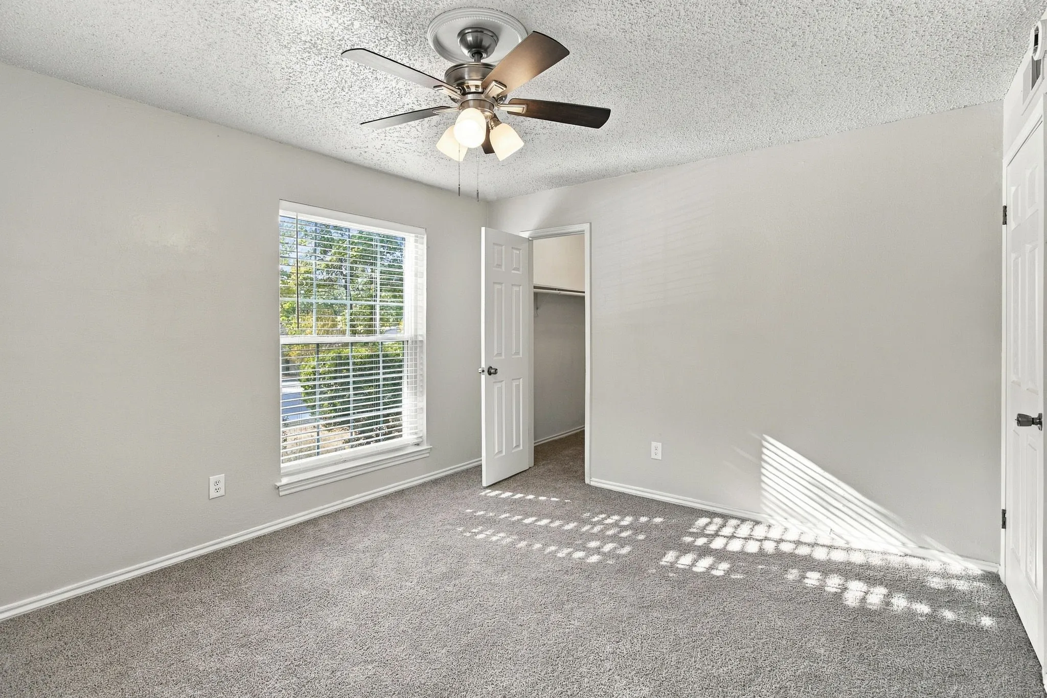Neutral gray wall paint, textured ceiling, ceiling fan with integrated lighting, carpeted flooring, and a window with blinds