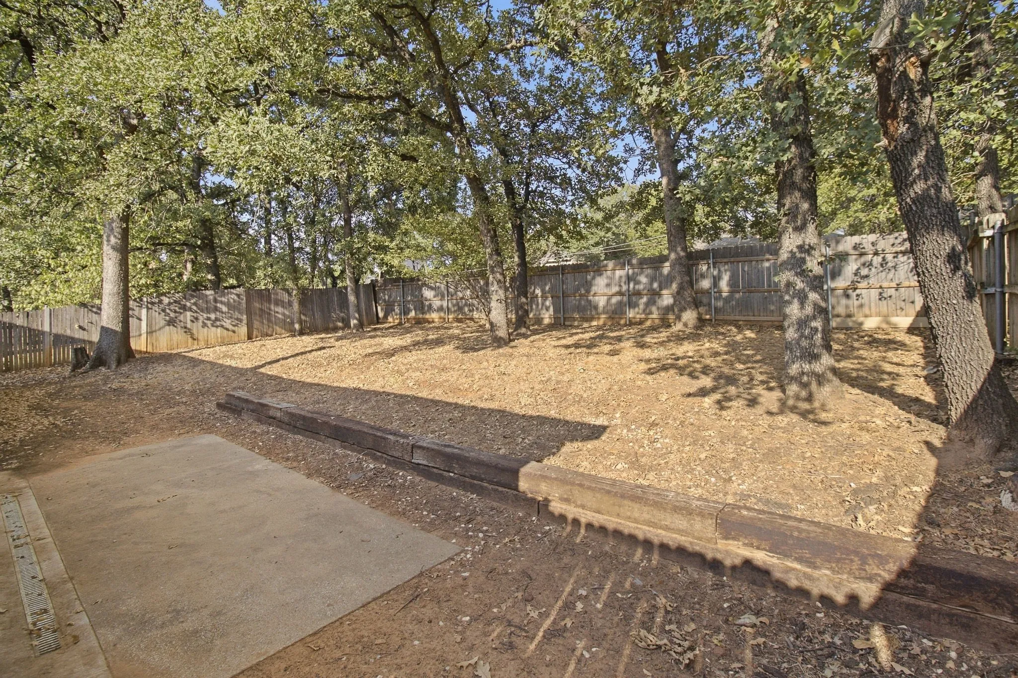 Backyard featuring mature trees, a wood privacy fence, and a concrete patio