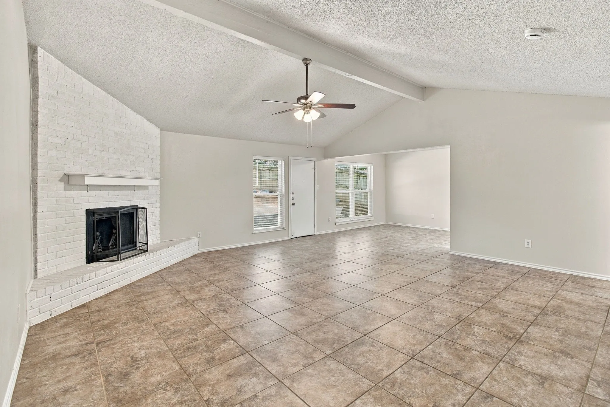 Vaulted ceiling, tiled flooring, painted brick fireplace with mantel, ceiling fan, and multiple windows