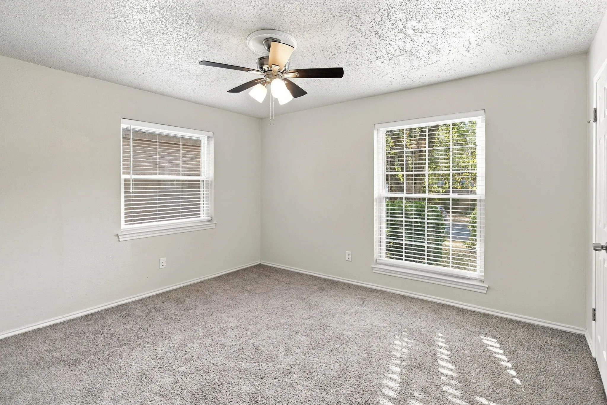 Wall-to-wall carpeting with light gray walls, two windows with blinds, and a ceiling fan with integrated lighting