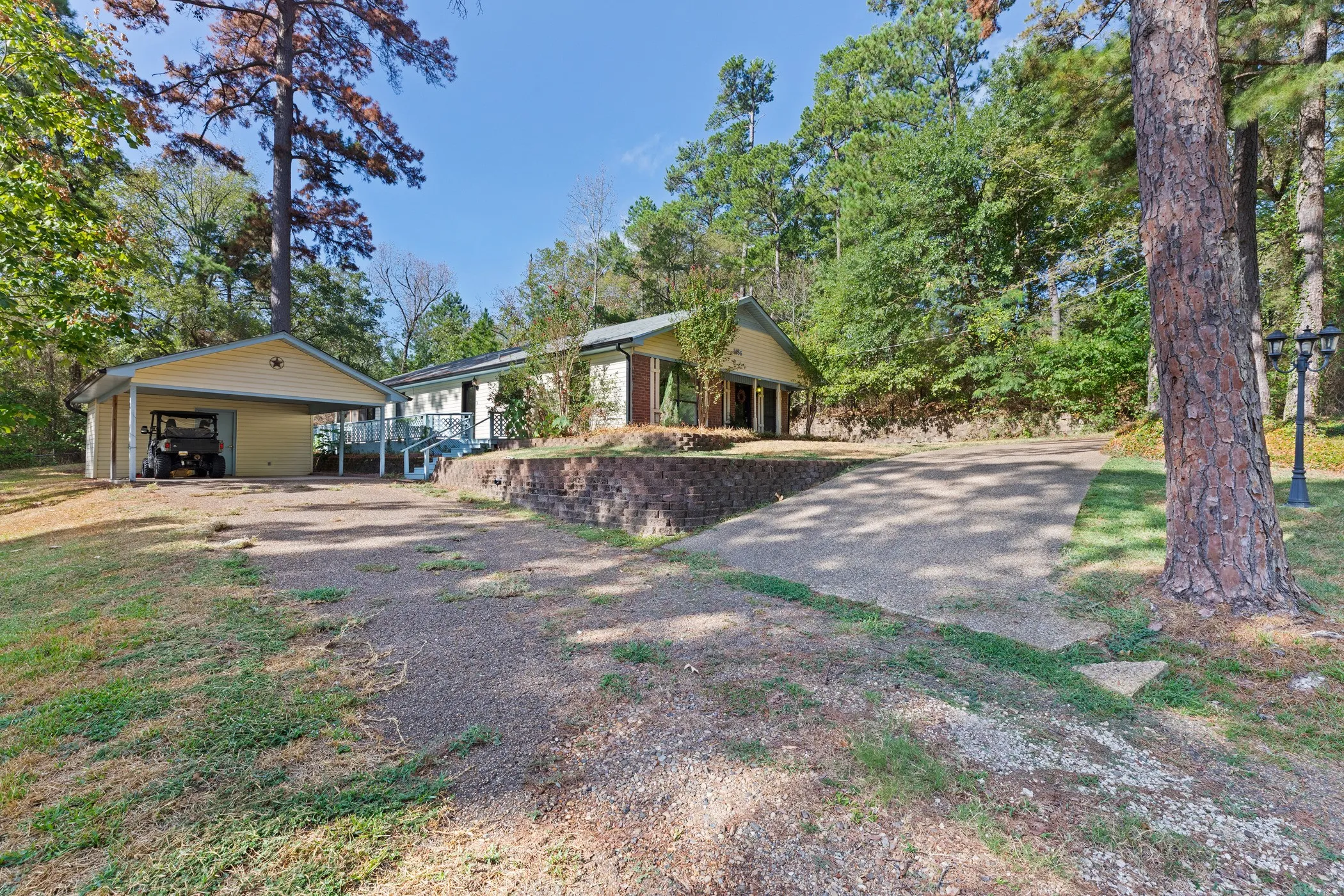 Detached carport with covered parking, elevated main residence, gravel driveway, and a retaining wall