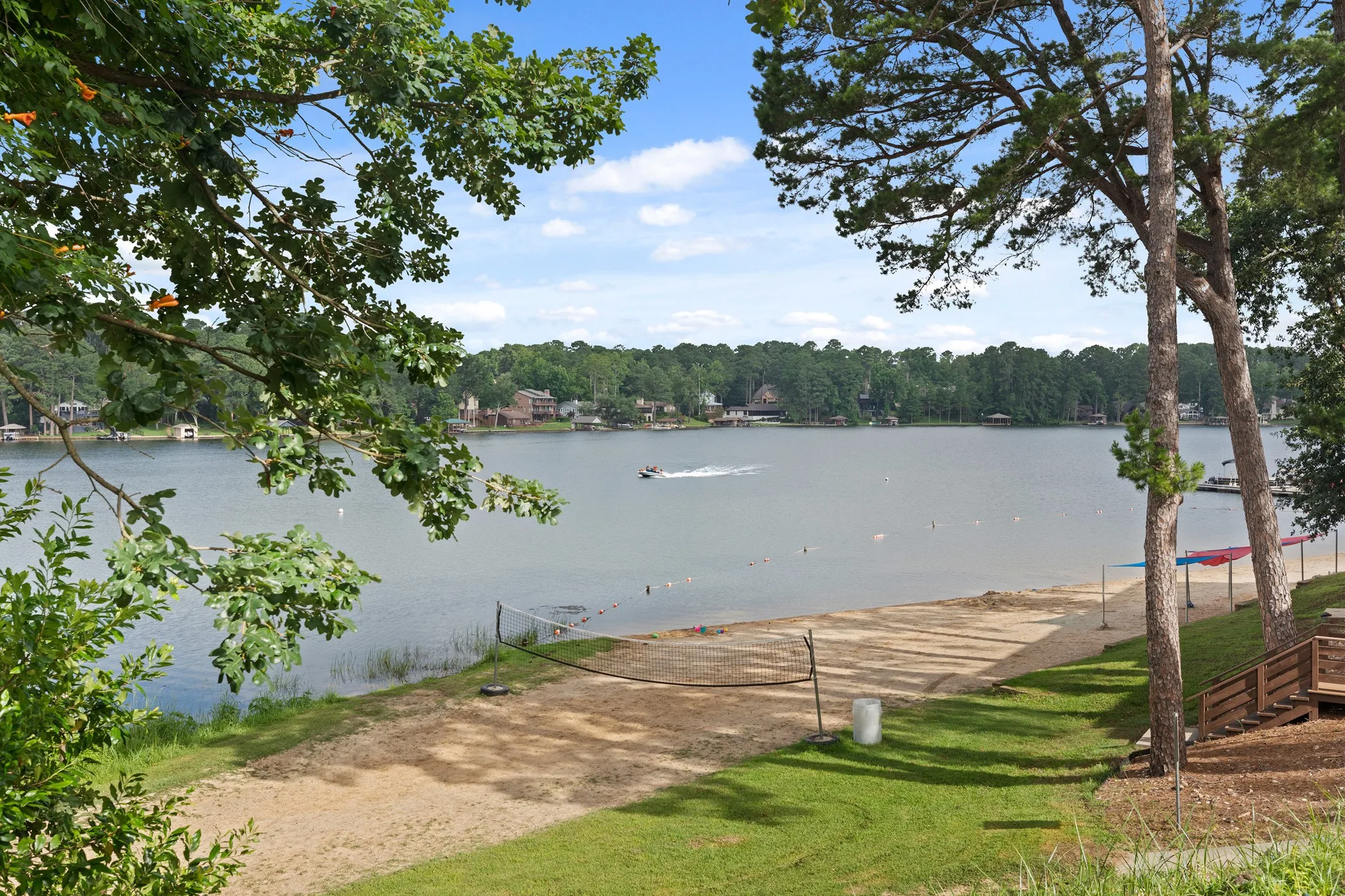 Expansive waterfront property featuring a sandy beach, mature trees, and a wooden staircase