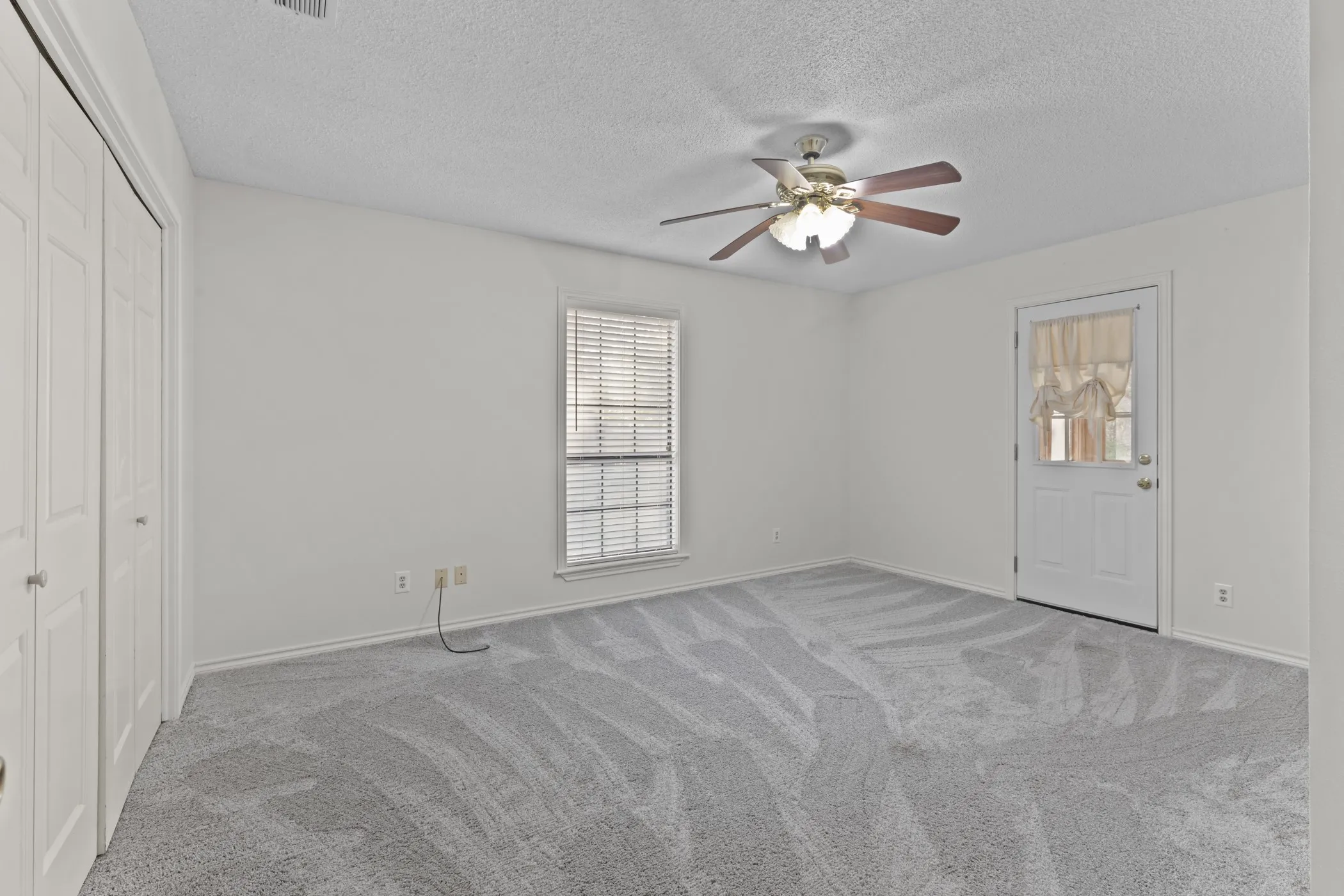 Wall-to-wall carpeting, ceiling fan with integrated lighting, glass-paneled door, and louvered window blinds