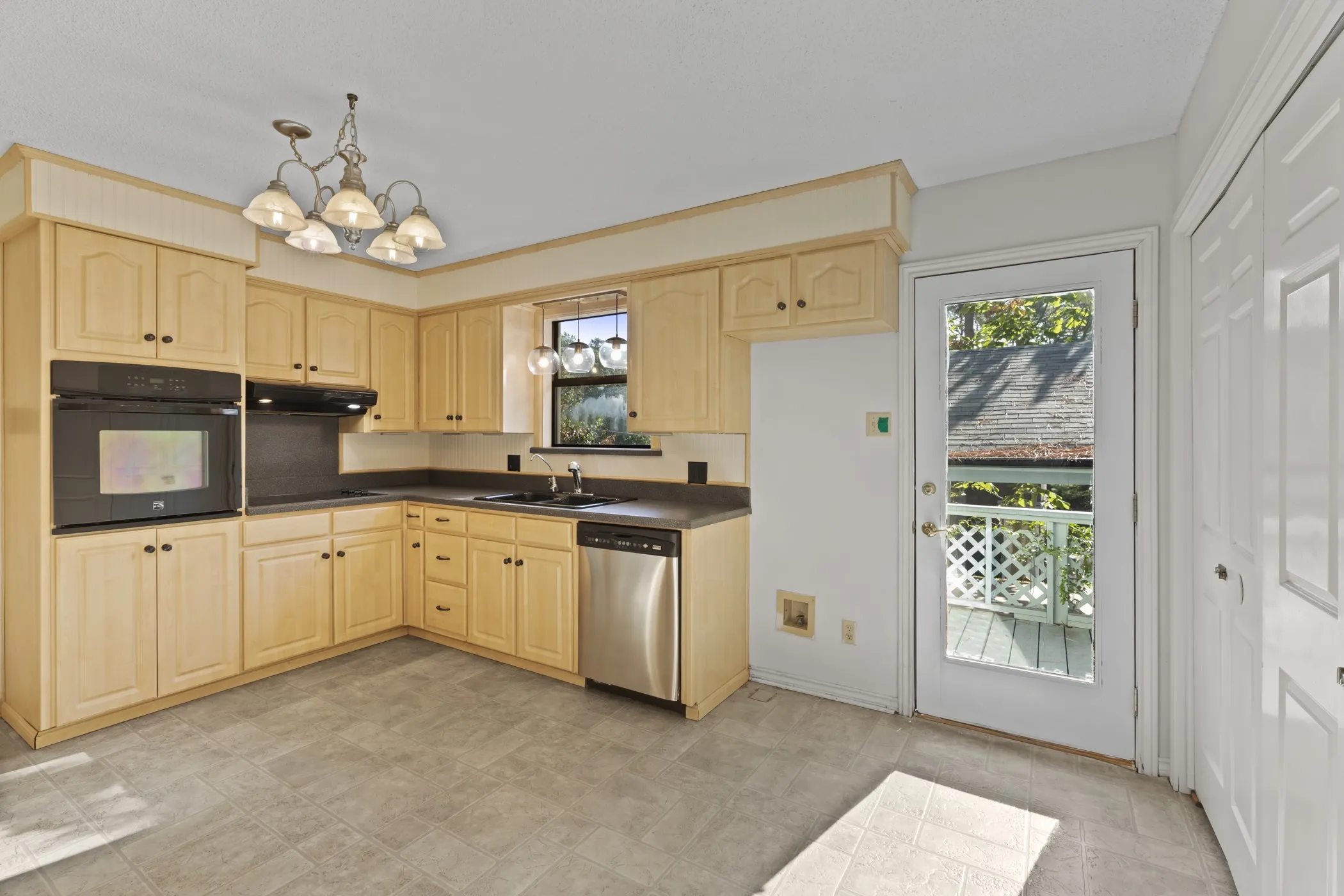 L-shaped kitchen featuring wood cabinetry, built-in oven, stainless steel dishwasher, and a glass-paned door