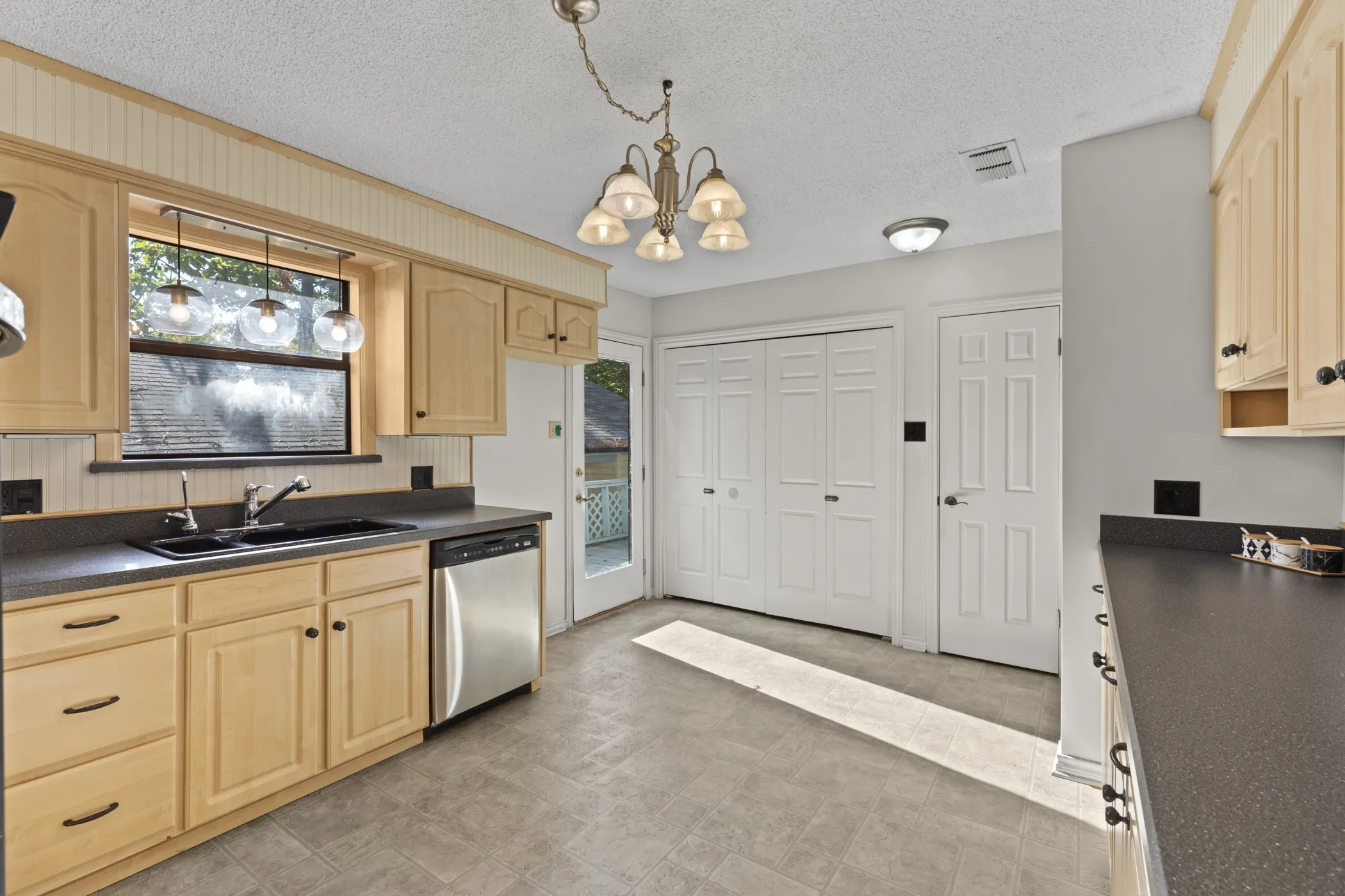 Light wood-finish cabinetry with dark hardware, stainless steel dishwasher, dark countertops, and a double-basin sink