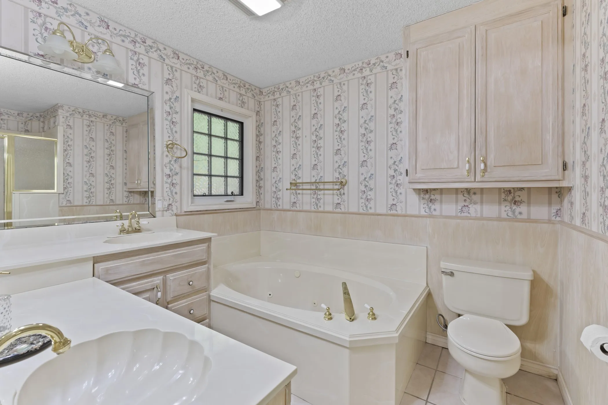 Dual vanity with shell-shaped basin, corner soaking tub, integrated toilet, and built-in upper cabinetry