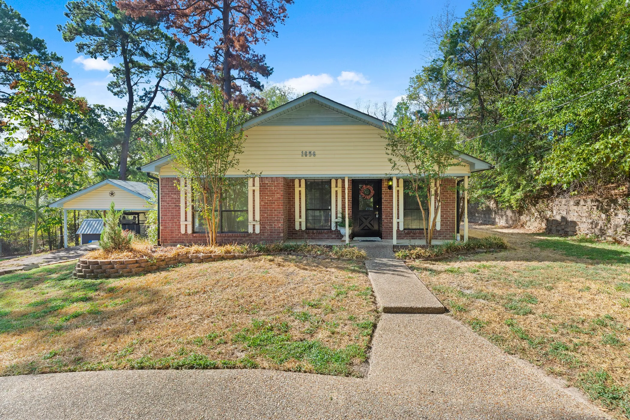 Brick and siding facade with a covered front porch, concrete walkway, and a detached carport