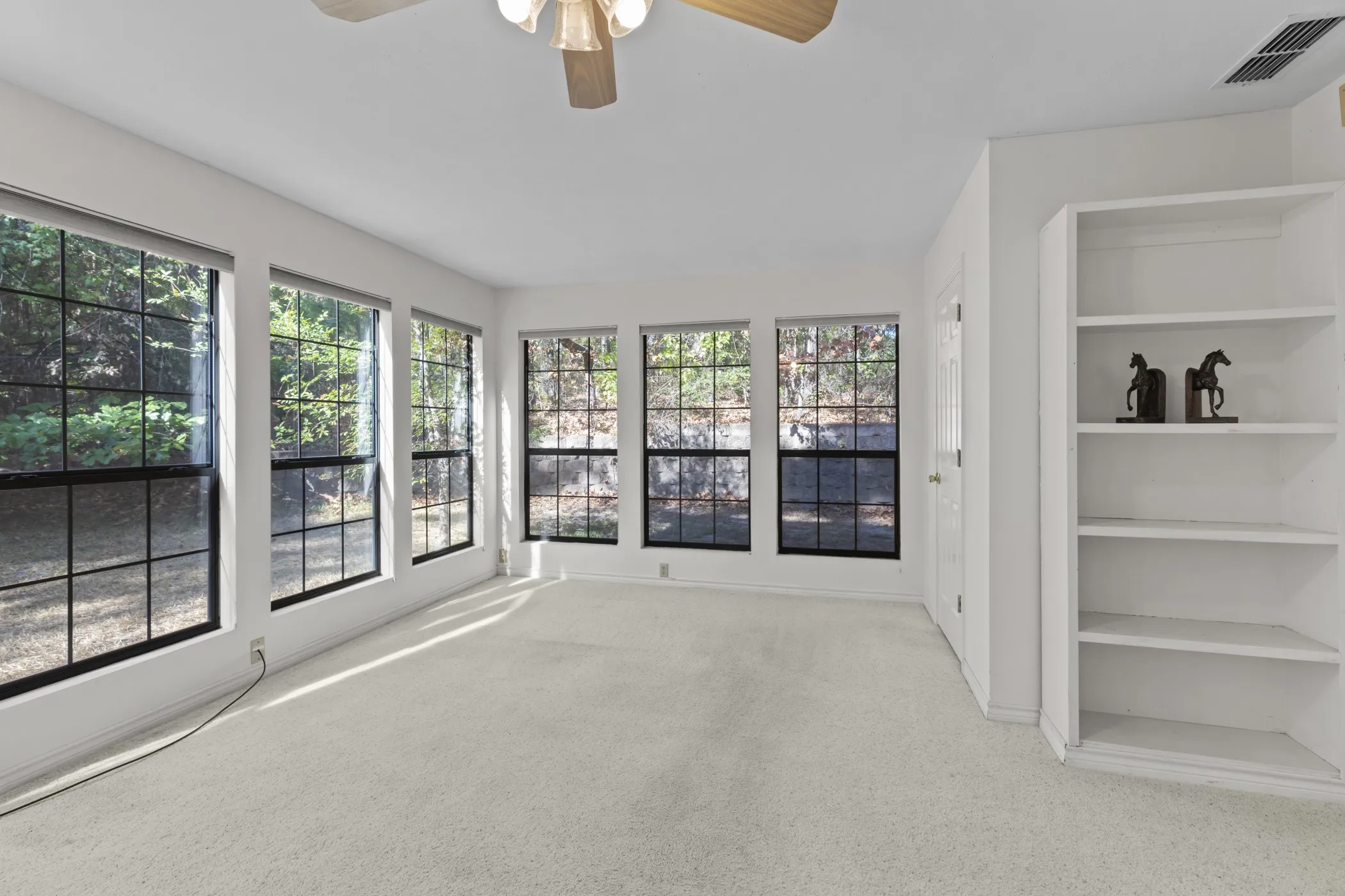 Wall-to-wall carpeting, multiple large windows with grids, built-in shelving, ceiling fan, and white painted walls