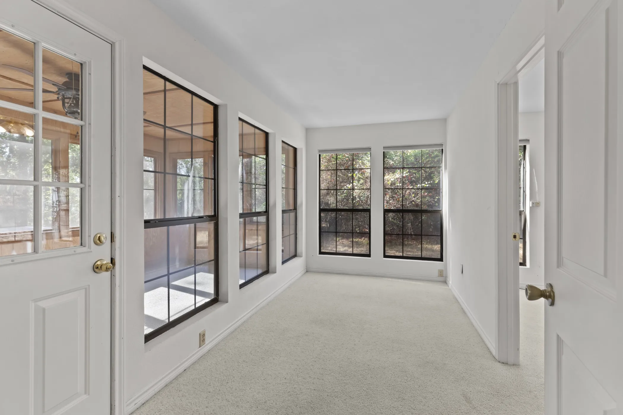 Crisp white walls, neutral carpeting, multiple windows with black grilles, and a white paneled door with brass hardware