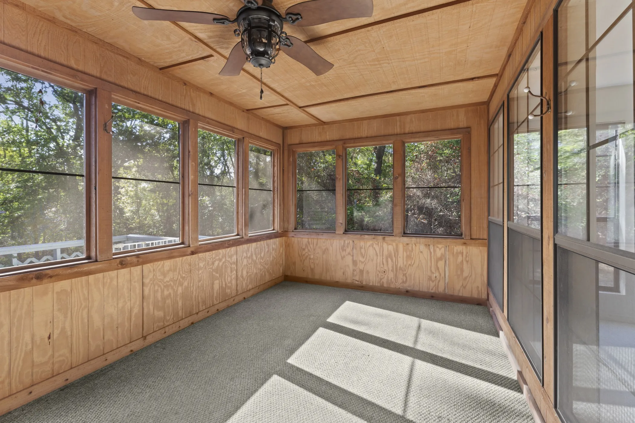 Sunroom featuring wood paneling, multiple windows, a ceiling fan, and carpeted flooring