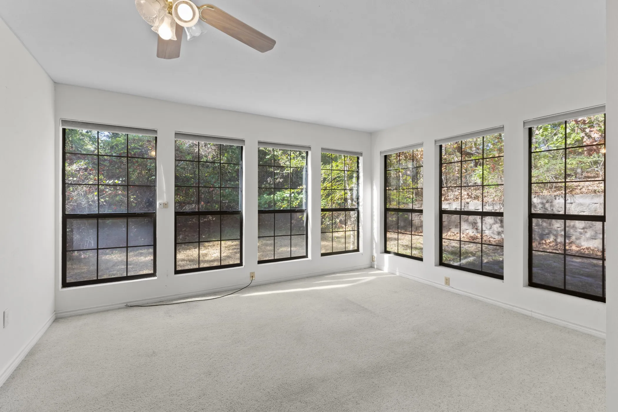 Recessed windows with black grilles, white walls, light-colored carpeting, and a ceiling fan with integrated lighting