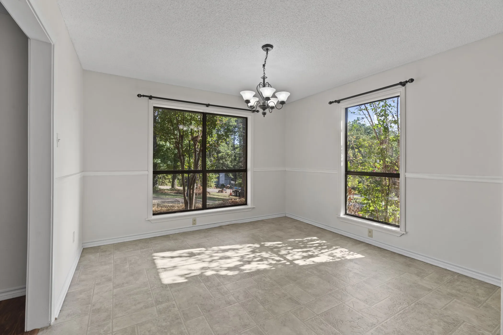 Recessed lighting with a ceiling-mounted chandelier, paired with two large windows, white wall paneling, and tile flooring