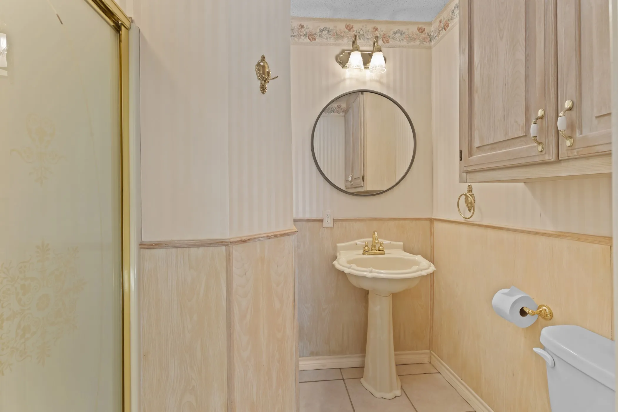 Pedestal sink, wall-mounted vanity light, round mirror, built-in cabinetry, and wainscoting