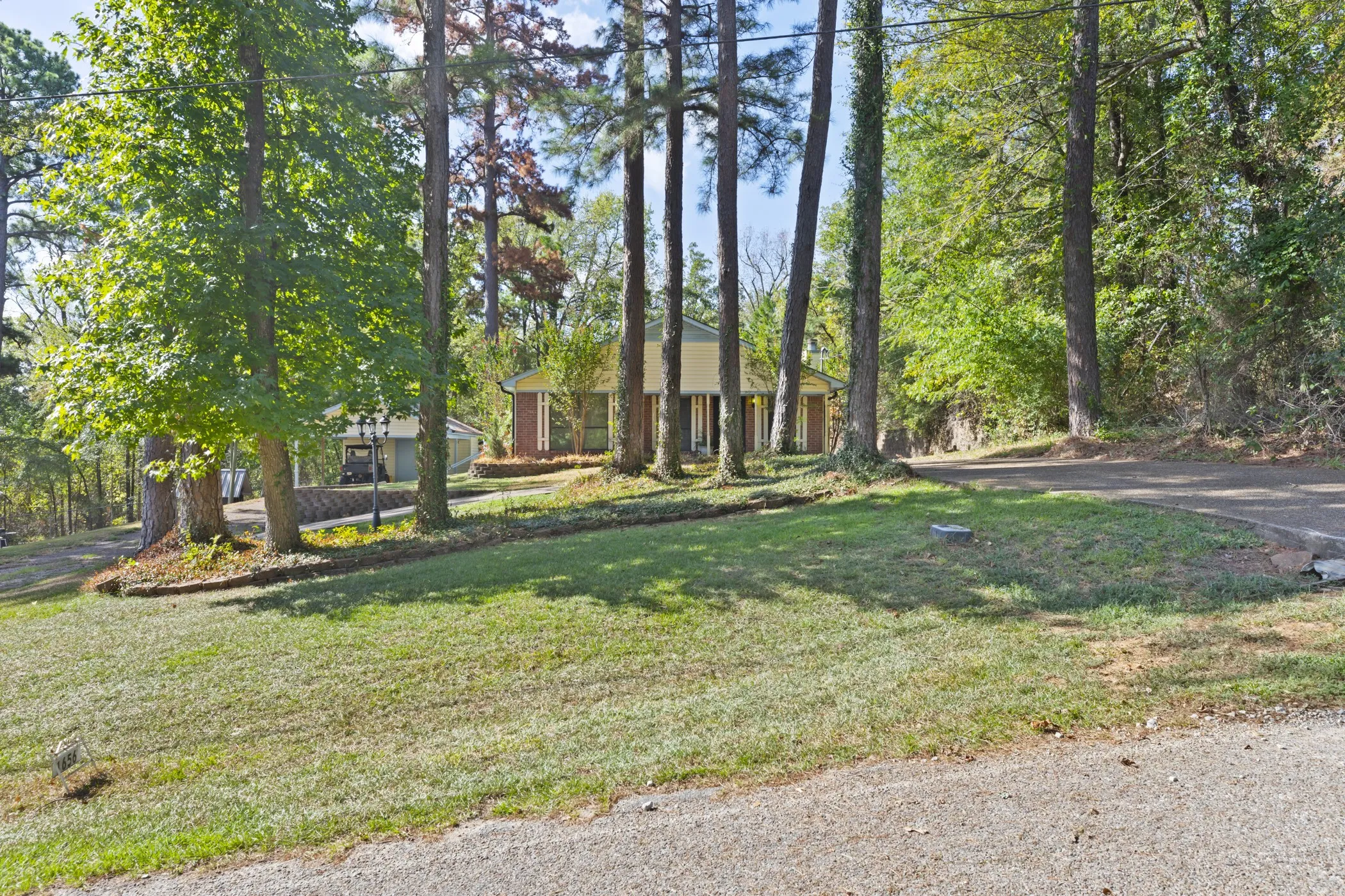 Mature trees, sloped grassy terrain, and a paved driveway leading to the property