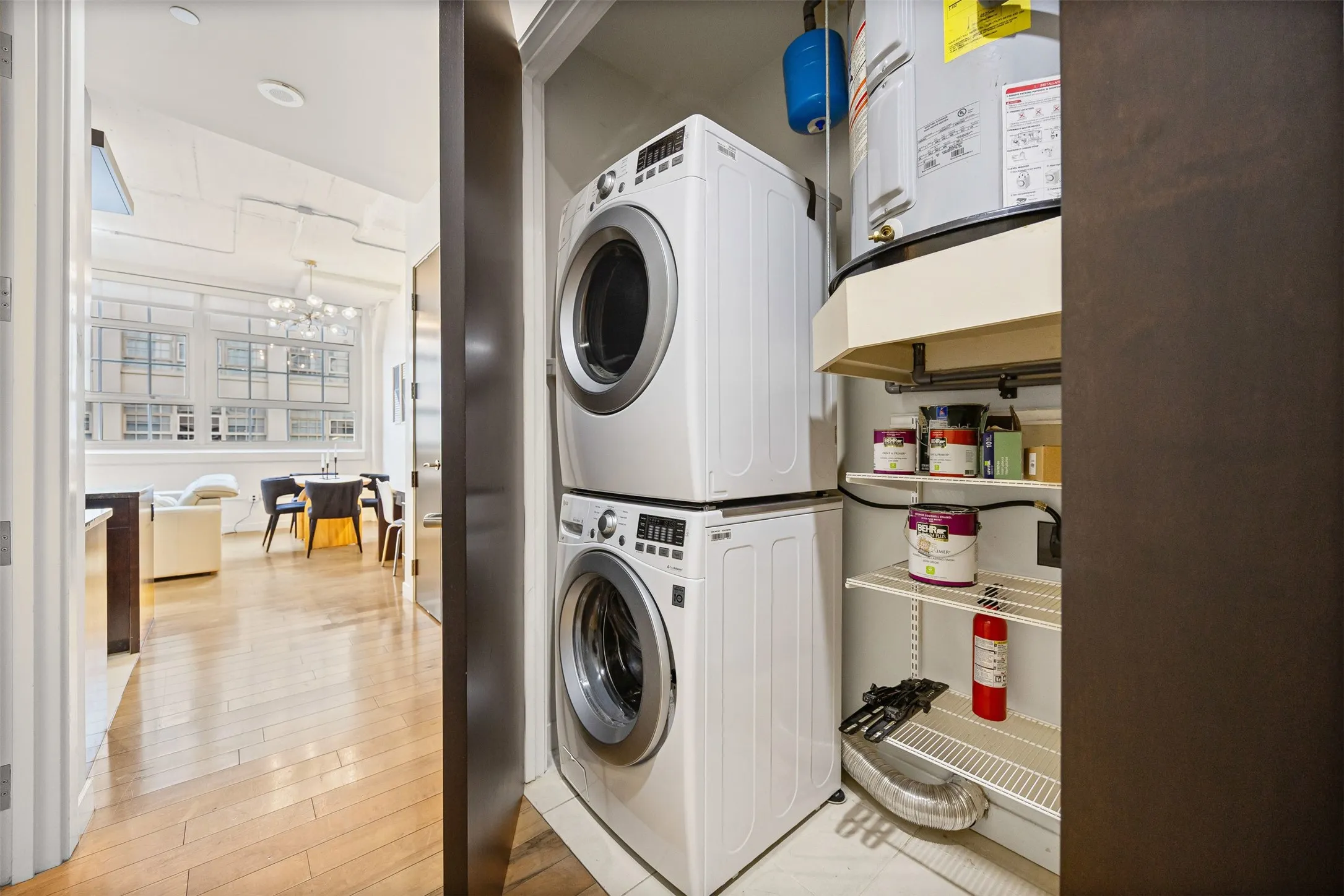 Laundry area with hanging lights, stacked washer / dryer, light wood-style flooring, and water heater