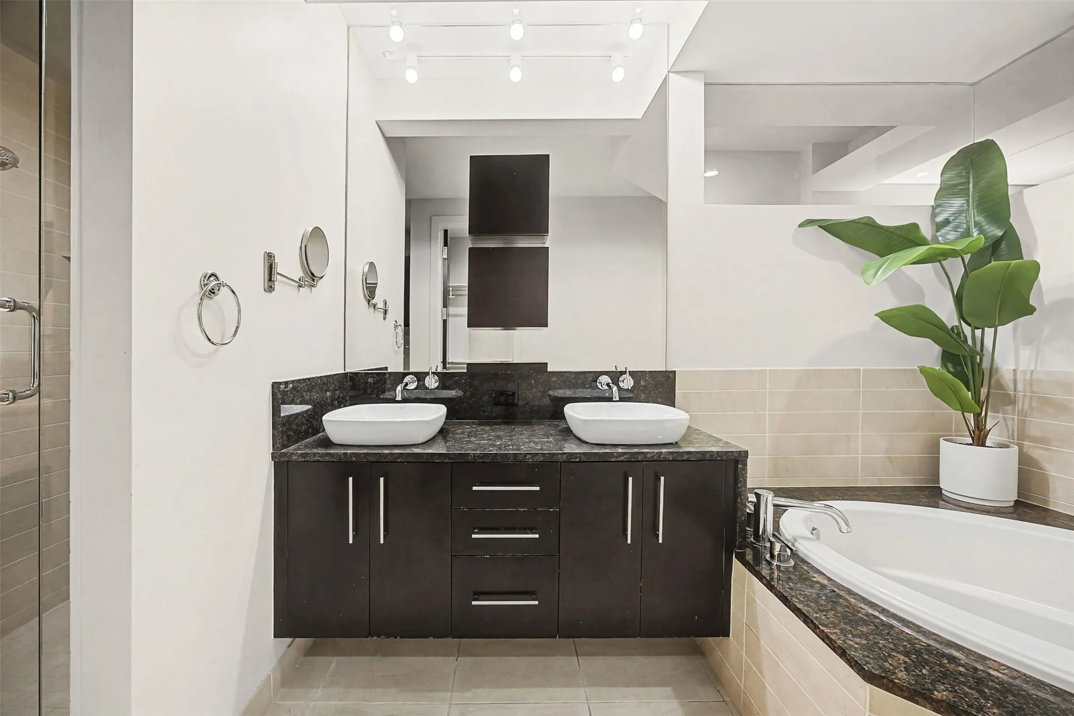 Full bath with double vanity, a garden tub, a stall shower, rail lighting, and light tile patterned flooring