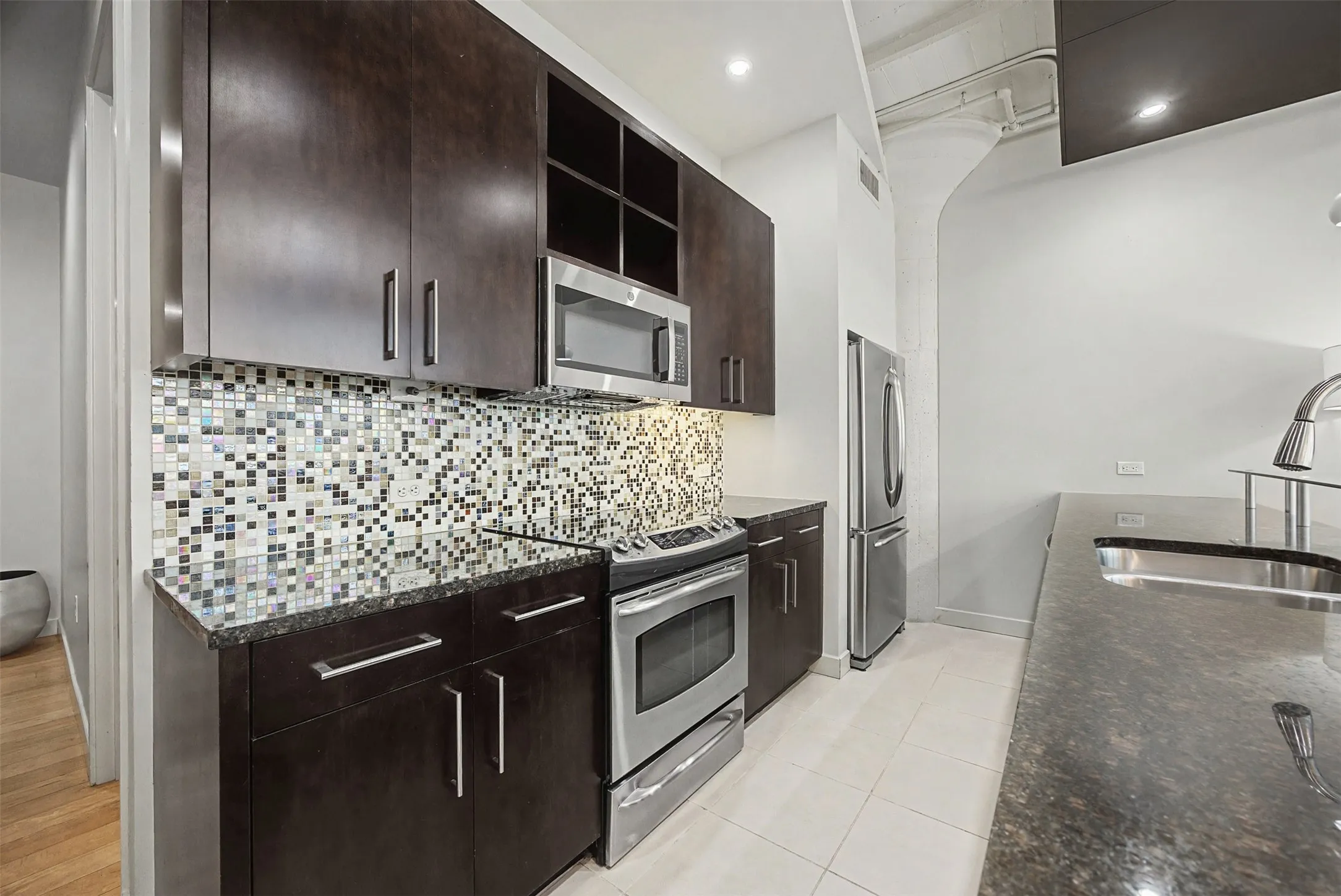 Kitchen featuring stainless steel appliances, open shelves, dark wood finish cabinets, dark stone counters, and recessed lighting