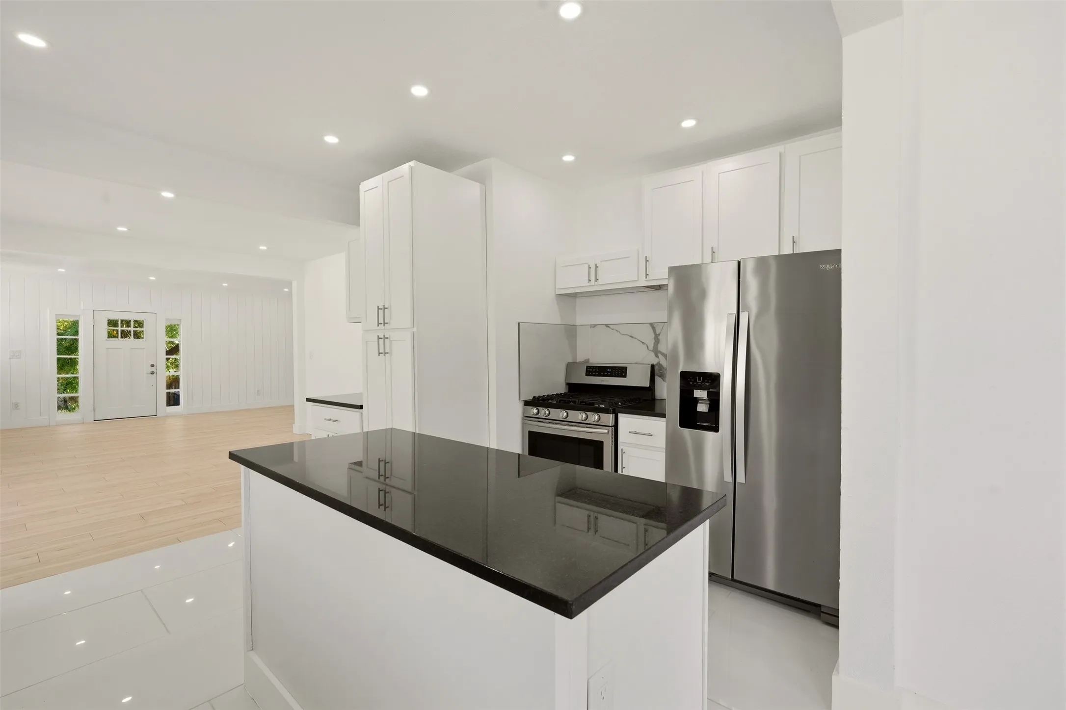 Kitchen featuring white cabinetry, stainless steel appliances, a center island with a dark countertop, and a white tile floor