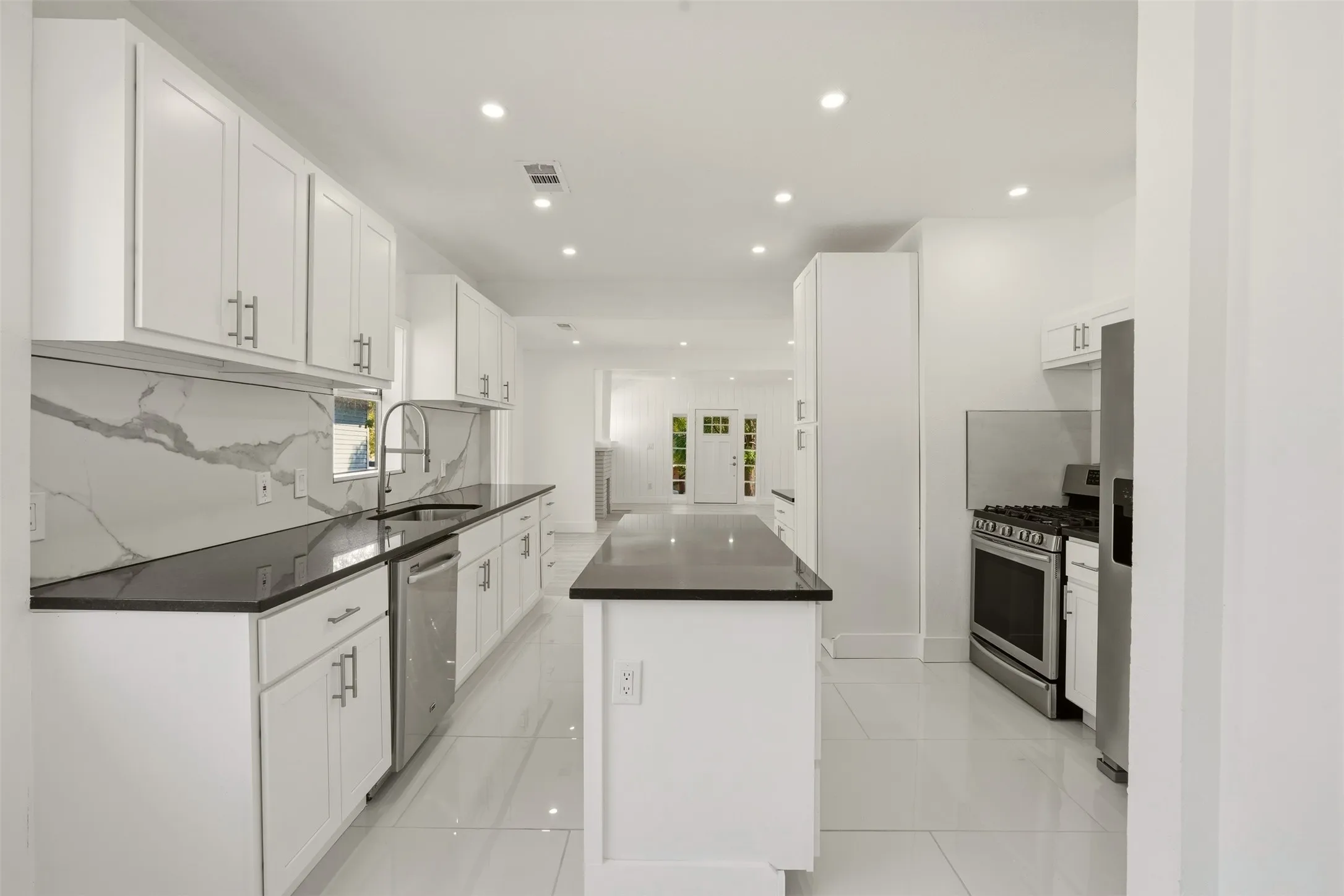 White shaker cabinetry, dark countertops, a large center island, stainless steel appliances, and recessed lighting