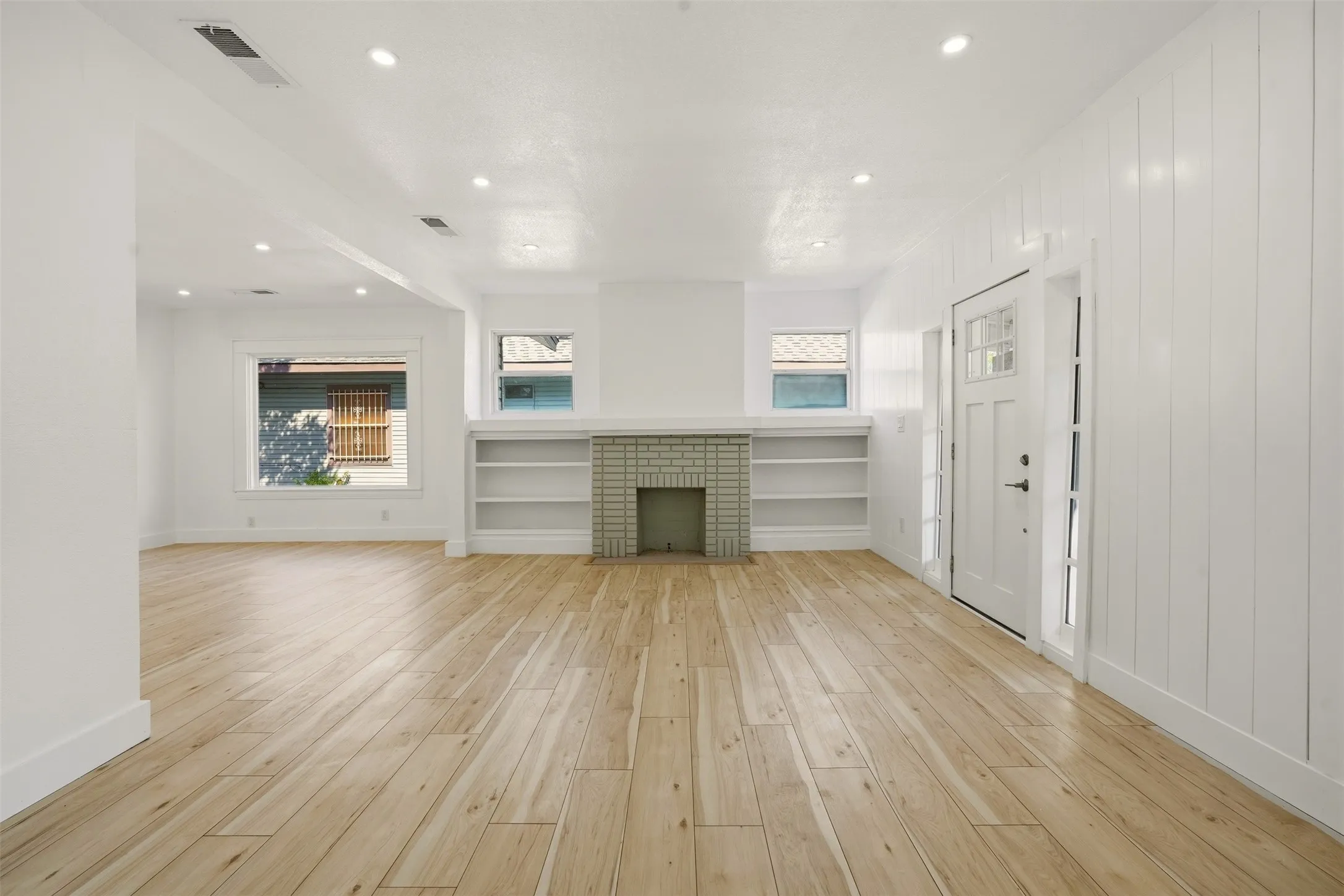 Recessed lighting throughout, wood-finish flooring, built-in shelving, tiled fireplace, and a front entry door with sidelights