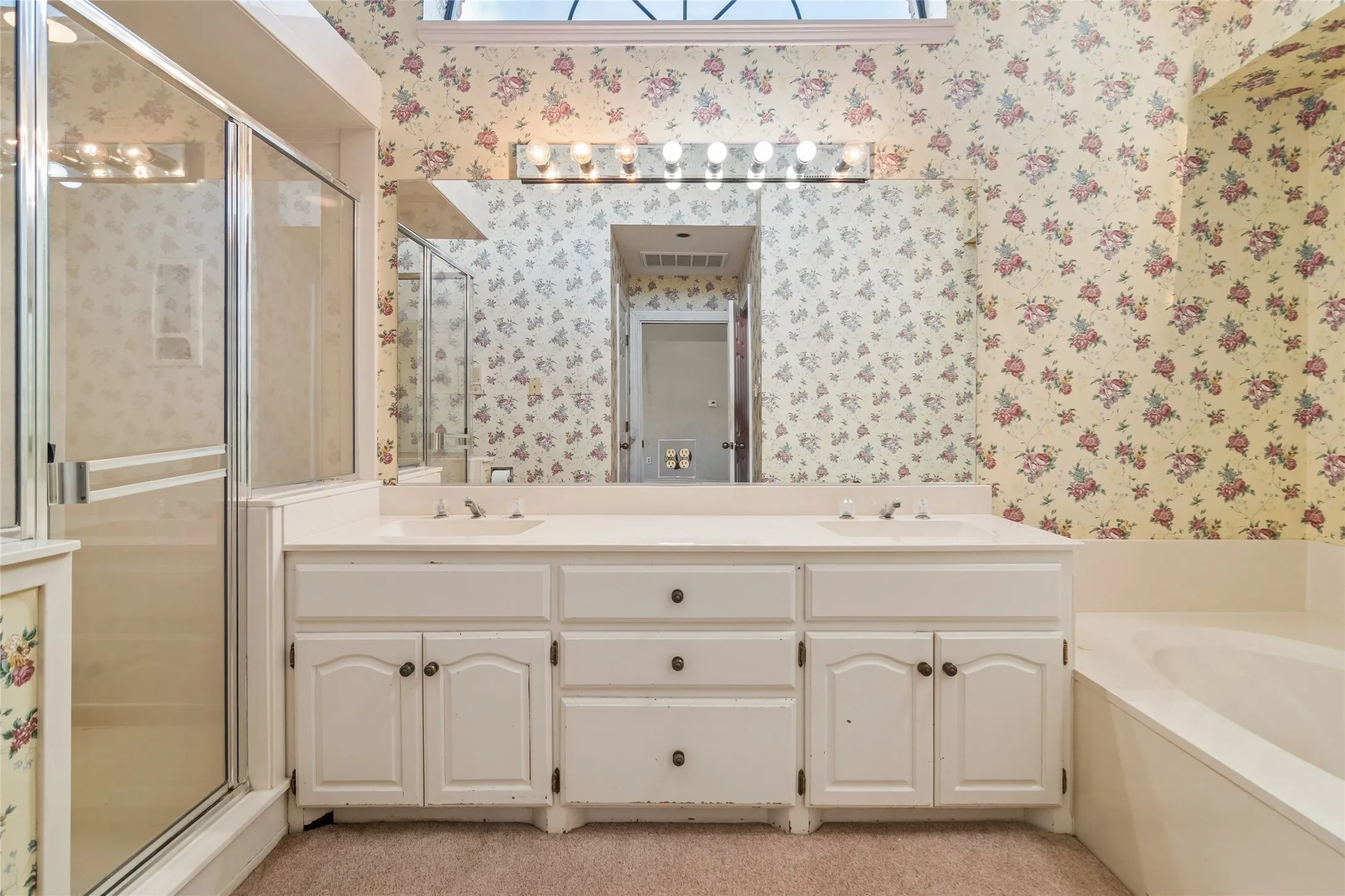 Dual sink vanity with white cabinetry, integrated mirror, and overhead lighting