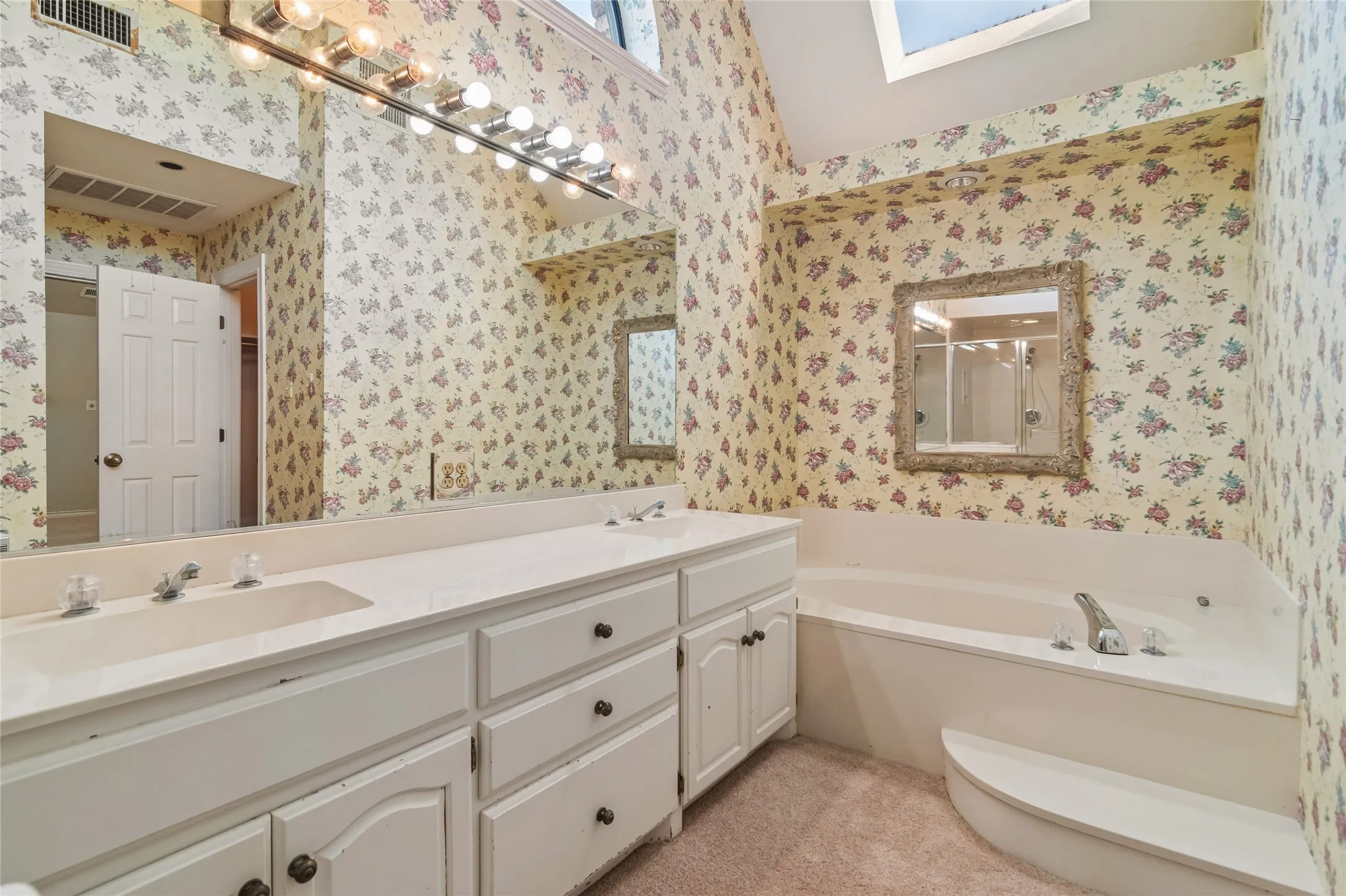 Primary Bathroom with two walk-in closets. Dual vanity with integrated sinks, built-in bathtub, and overhead skylight