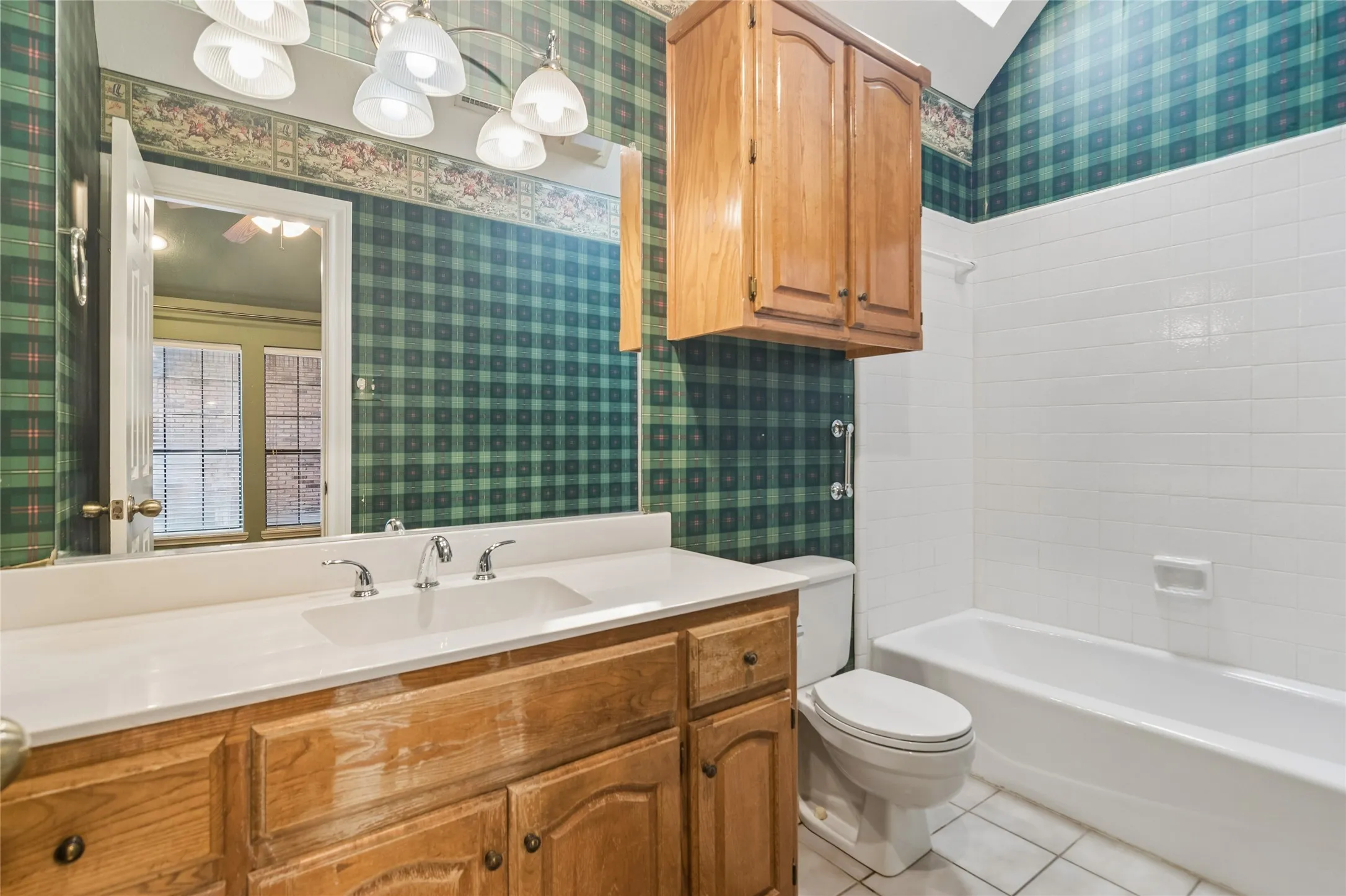 Single vanity with integrated sink, wood-finish cabinetry, chrome fixtures, and a drop-in bathtub with white tile surround