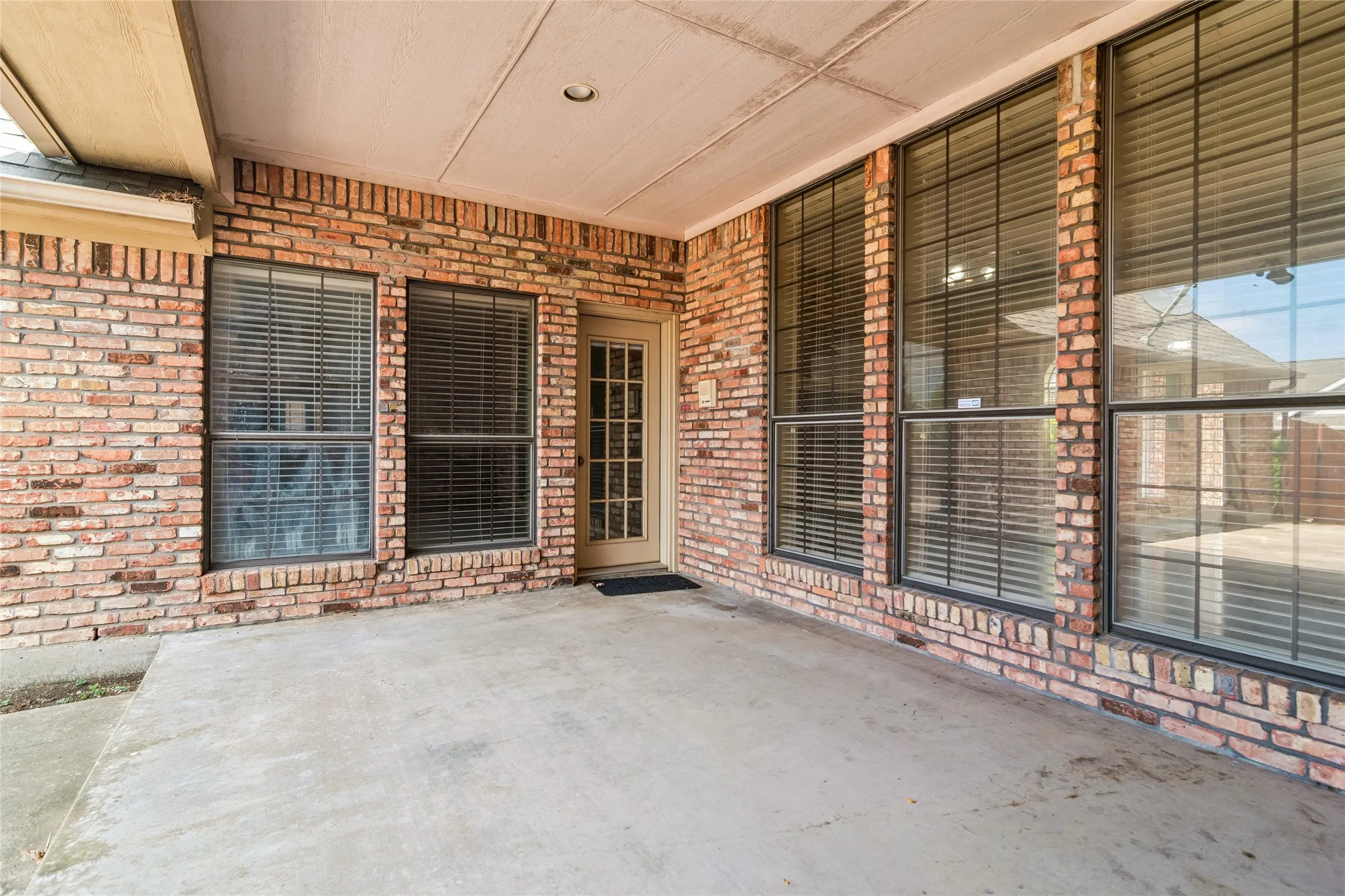 Covered patio with a concrete surface, brick exterior, multiple large windows with grids, and a French-style door
