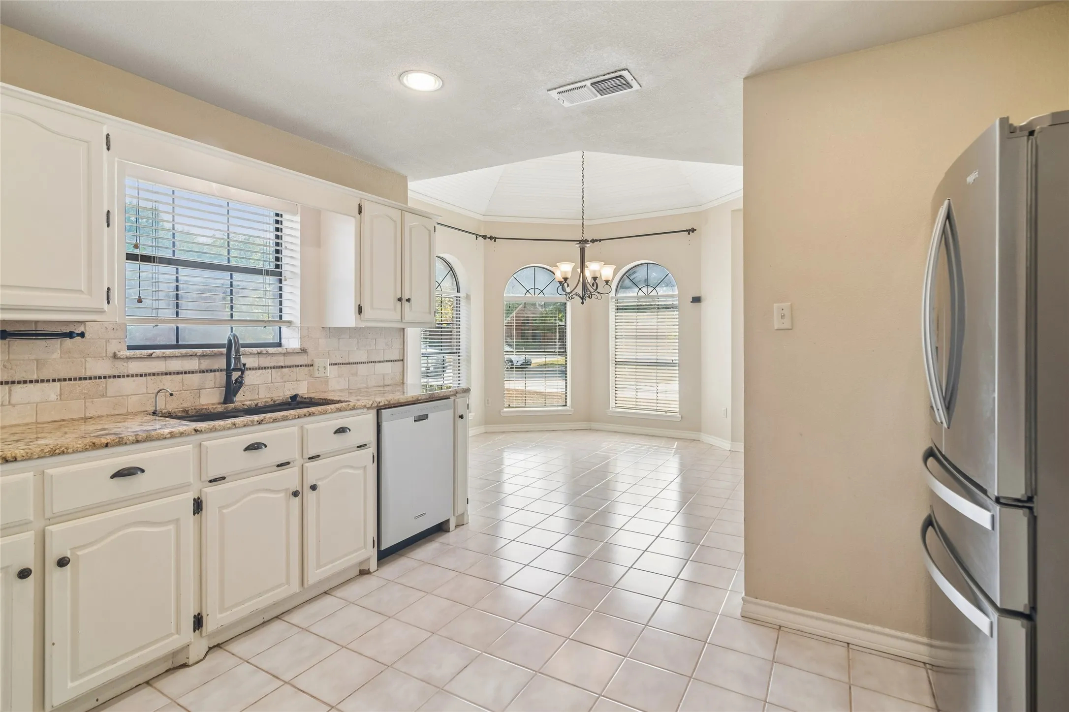 White cabinetry with black hardware, stone-finish countertops, and a tile backsplash