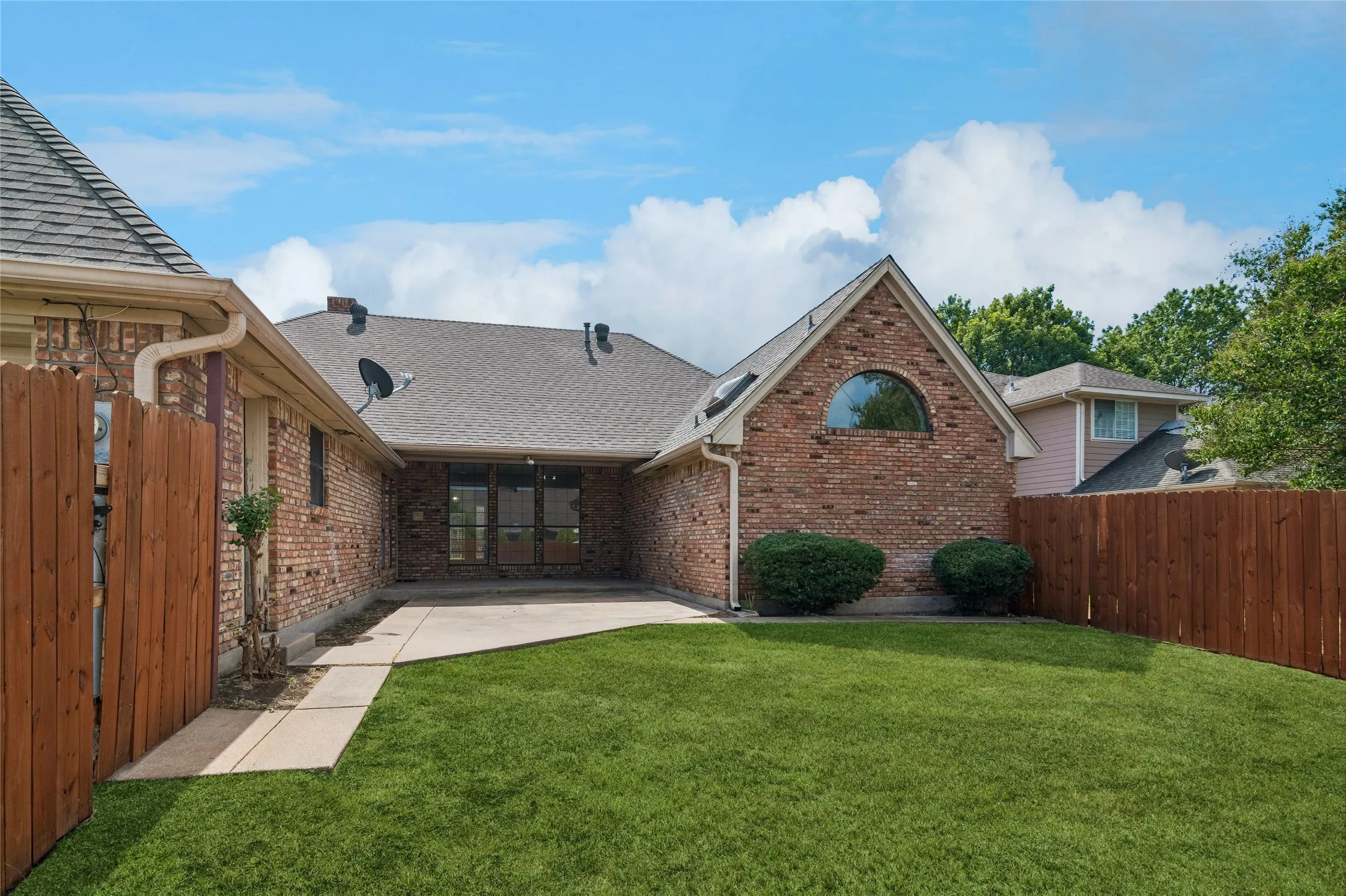 Brick exterior with an arched window, private fenced yard, and a concrete patio