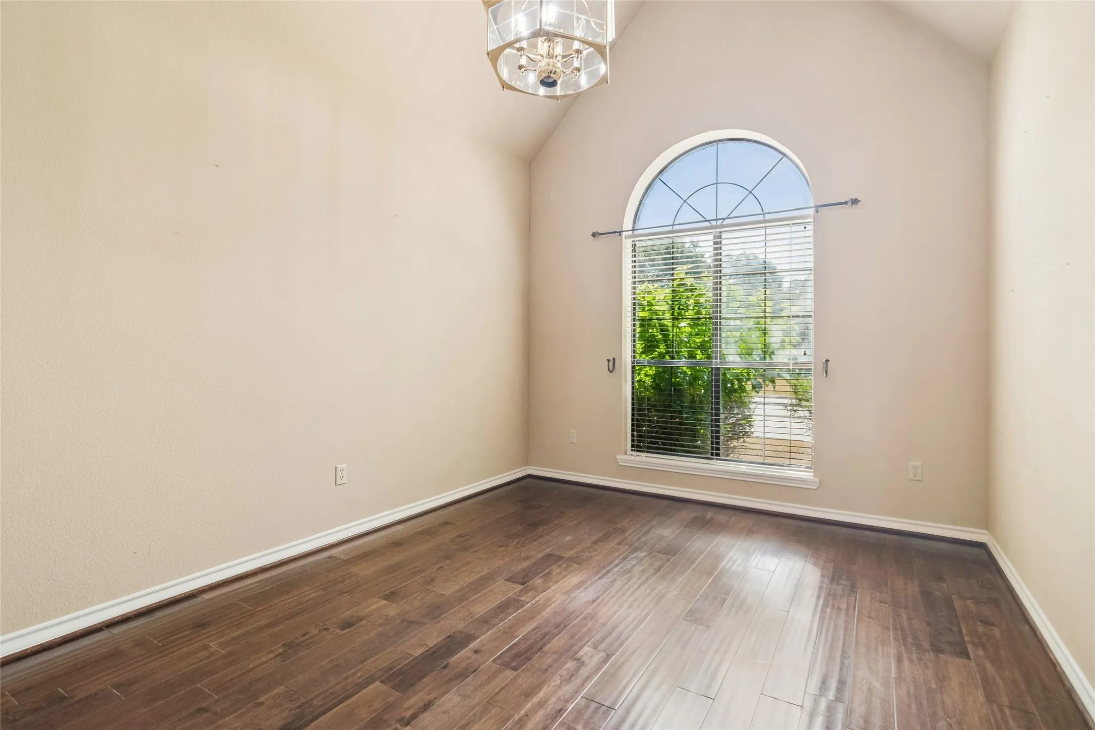 Vaulted ceiling with a decorative light fixture, arched window, and wood-finish flooring