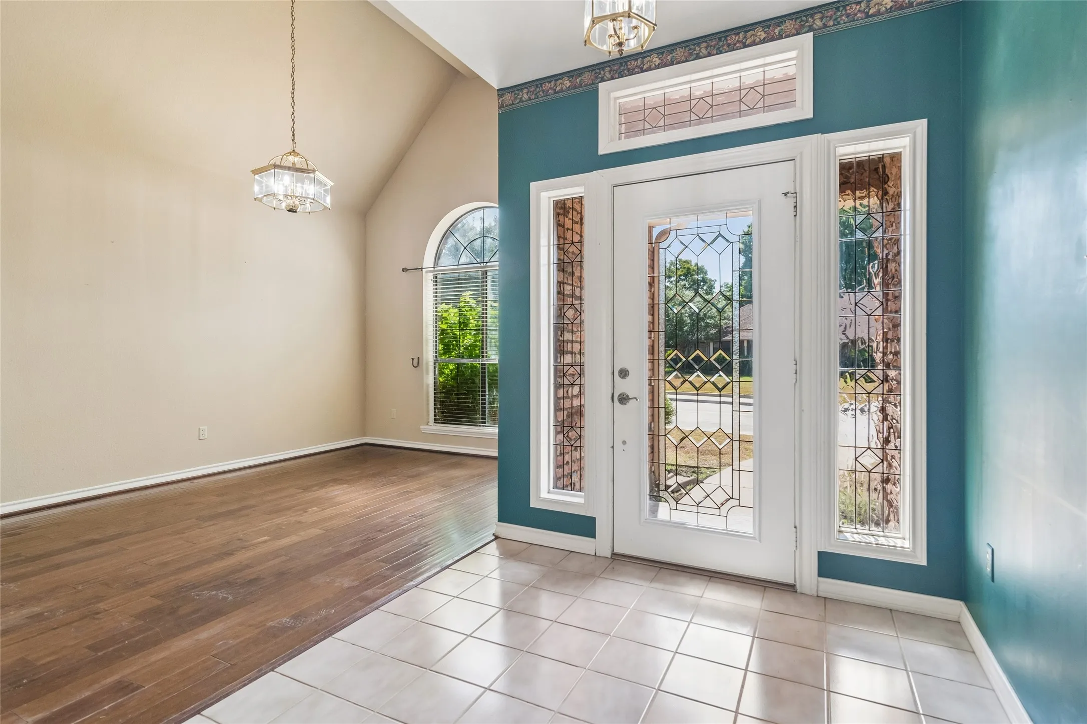 Entryway featuring a decorative glass door with sidelights and transom, tile flooring, and a vaulted ceiling with an overhead light fixture