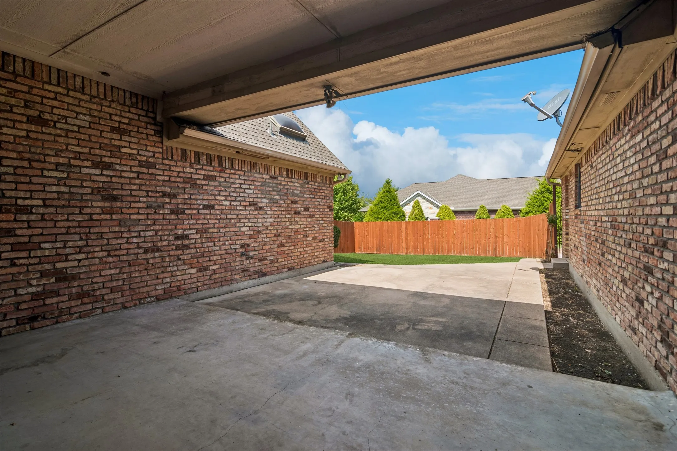 Covered carport with concrete flooring, brick exterior walls, and a wood-slat privacy fence