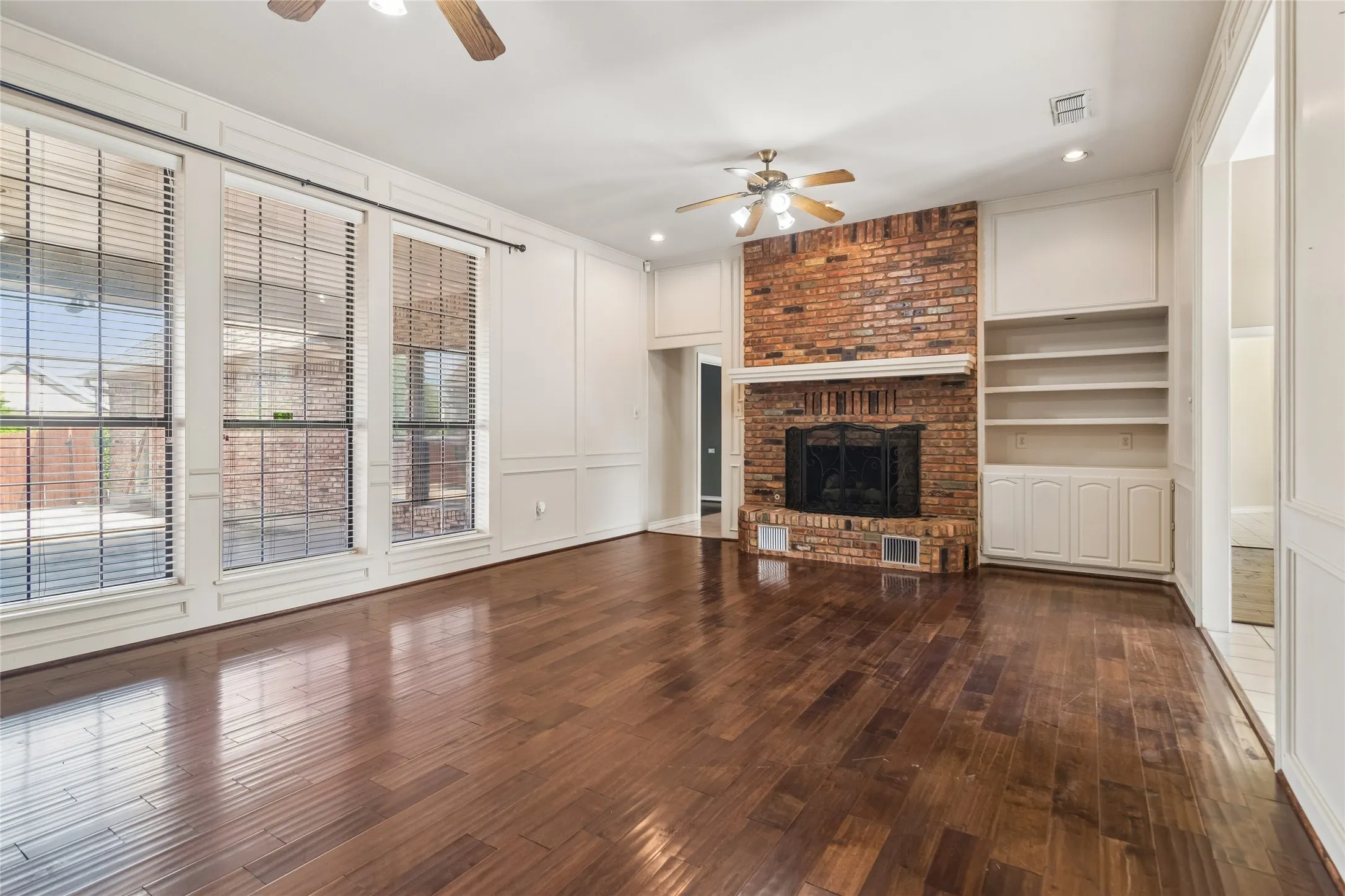 Dark wood-finish flooring, brick fireplace, built-in shelving, paneled walls, and multiple windows