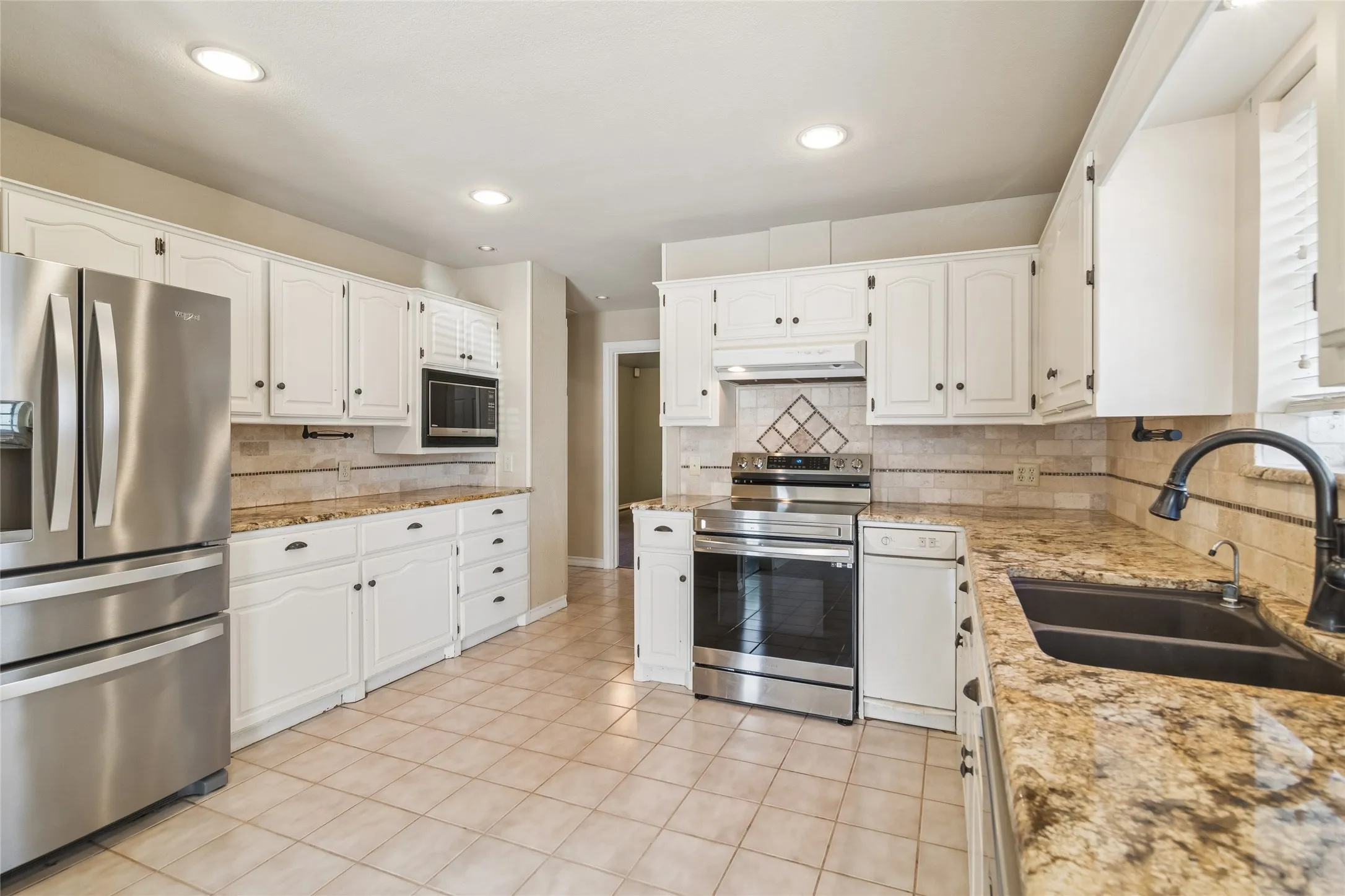 Kitchen featuring white cabinetry, granite countertops, stainless steel appliances, a tiled backsplash, and ceramic tile flooring