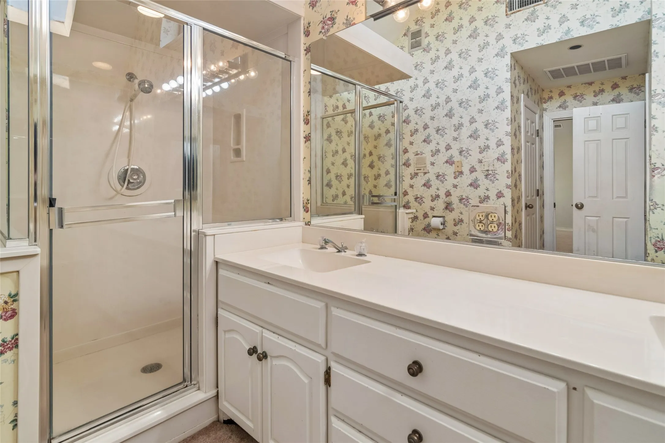 Shower enclosure with sliding glass door, white vanity with integrated sink, full-width mirror, and panel-front cabinetry with decorative hardware