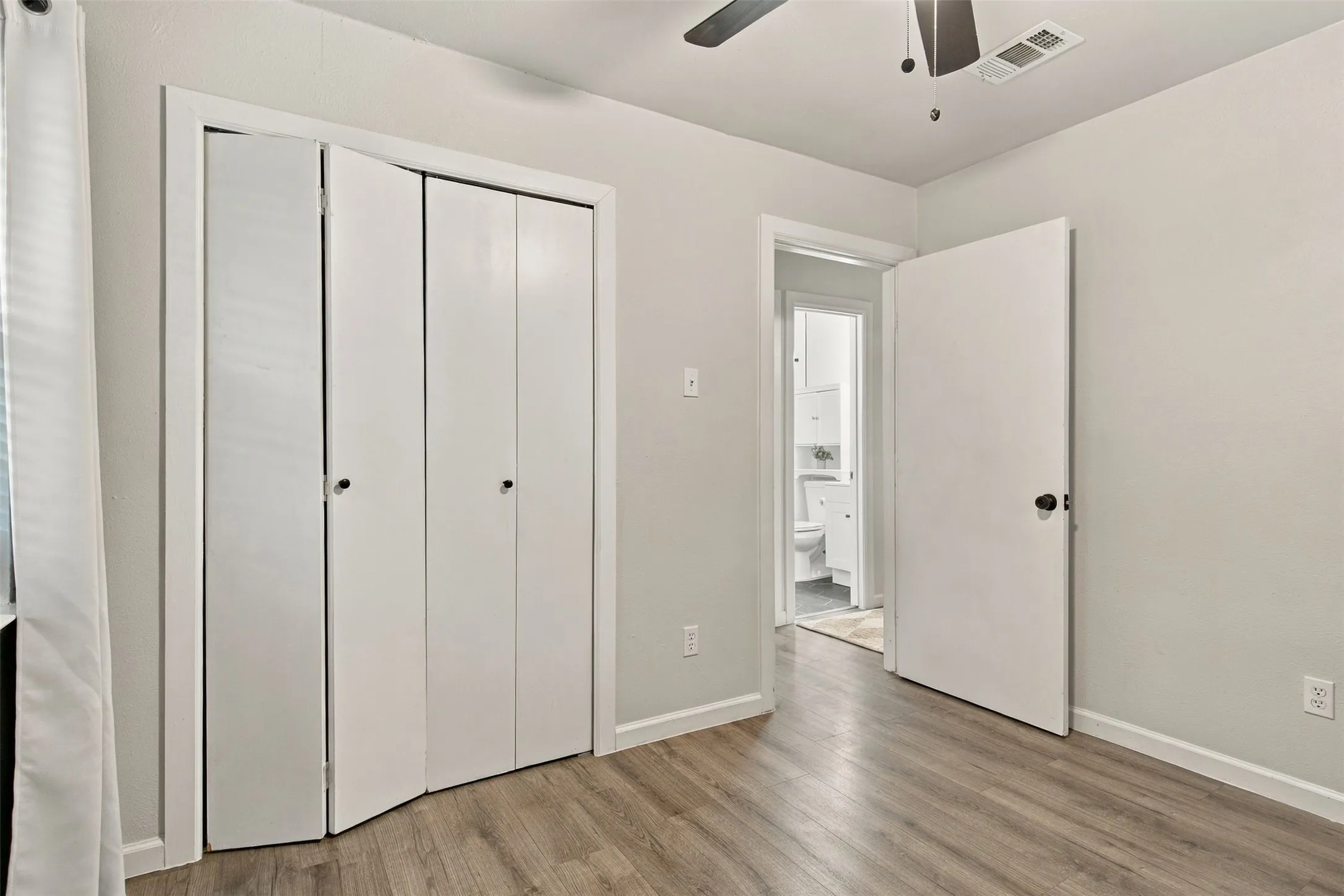 Wood-finish flooring, white bifold closet doors, light neutral wall paint, overhead ceiling fan, and white trim throughout